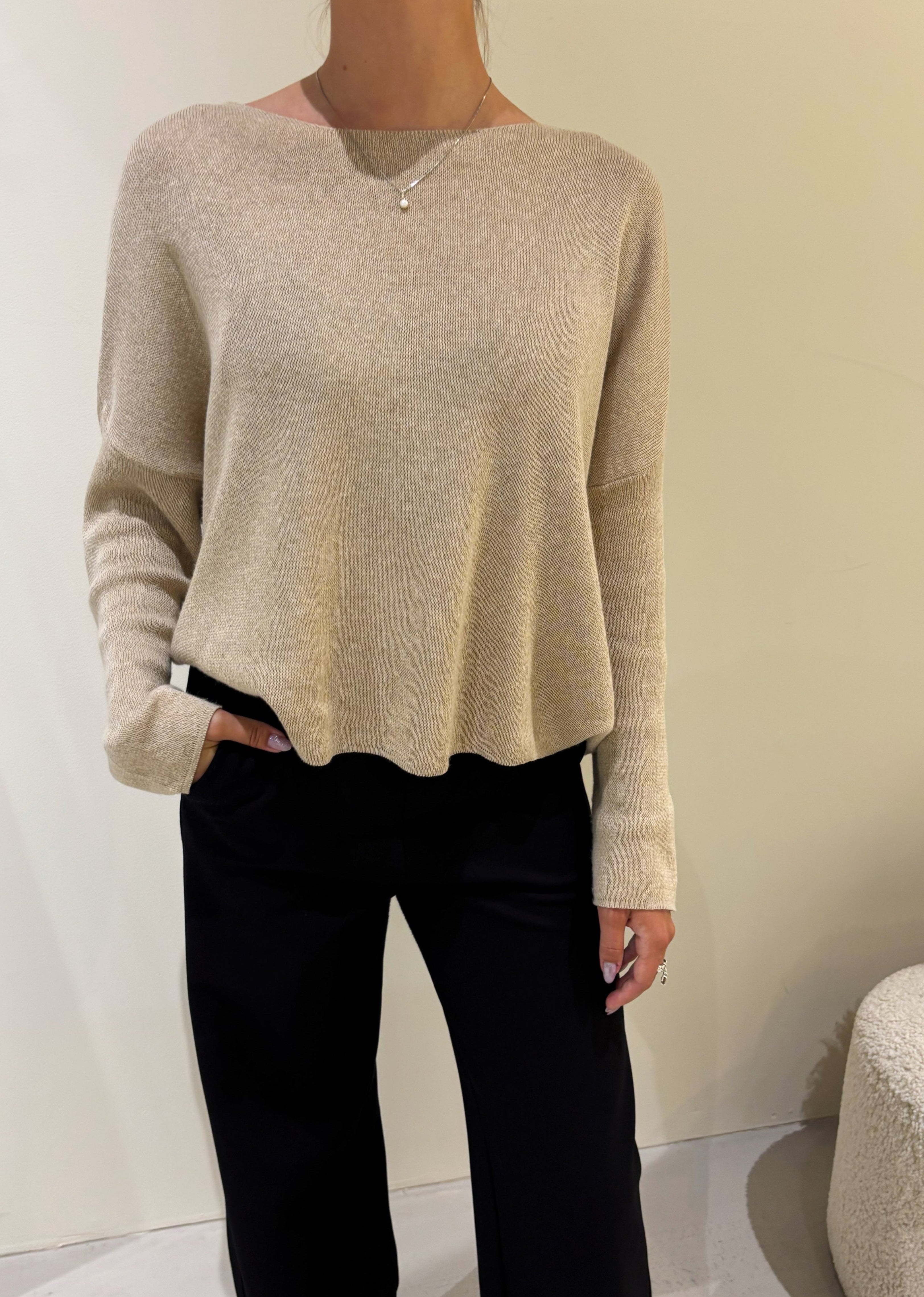 Person wearing a beige sweater and black pants against a plain background