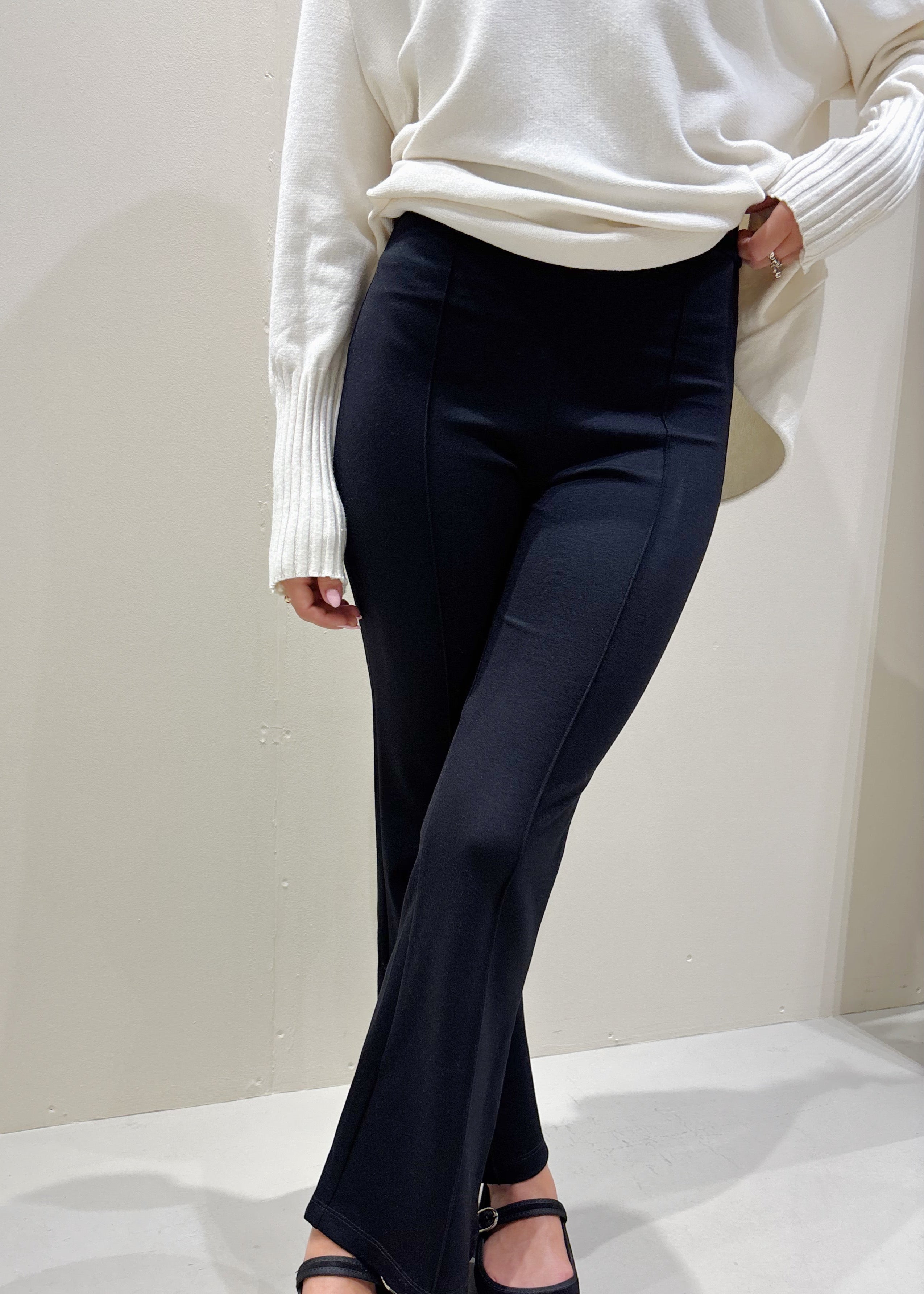 Person wearing navy flared pants and a white sweater on a white background