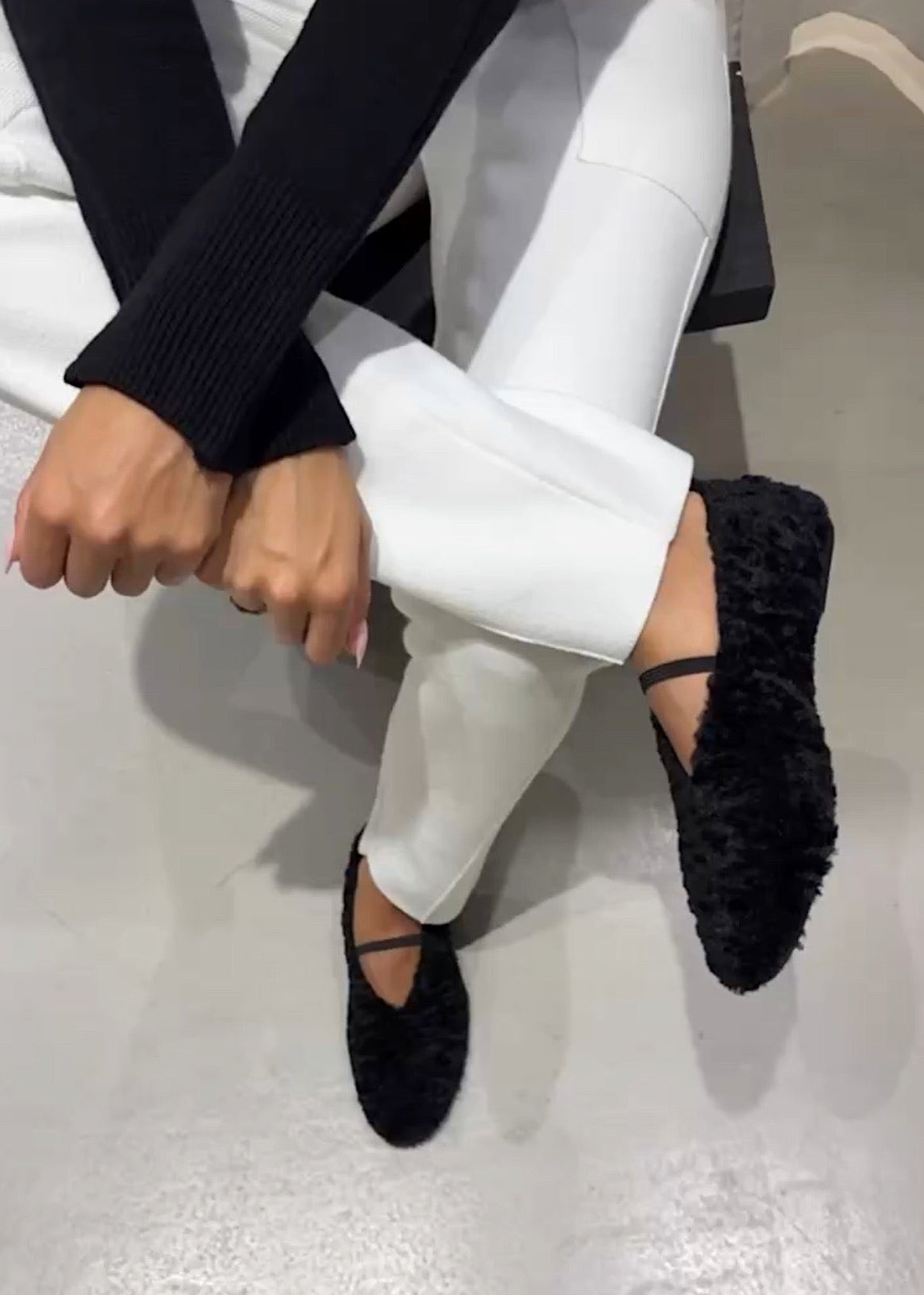 Person wearing black shoes and white pants sitting on a light gray floor.