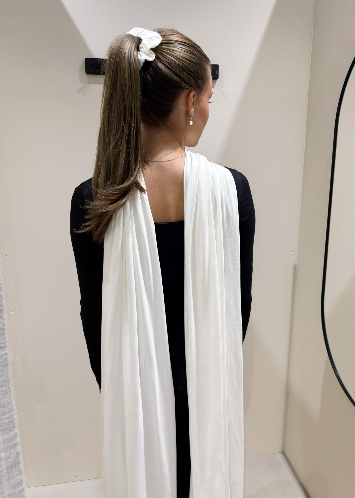 Woman wearing a white scarf, standing in a minimalistic room.