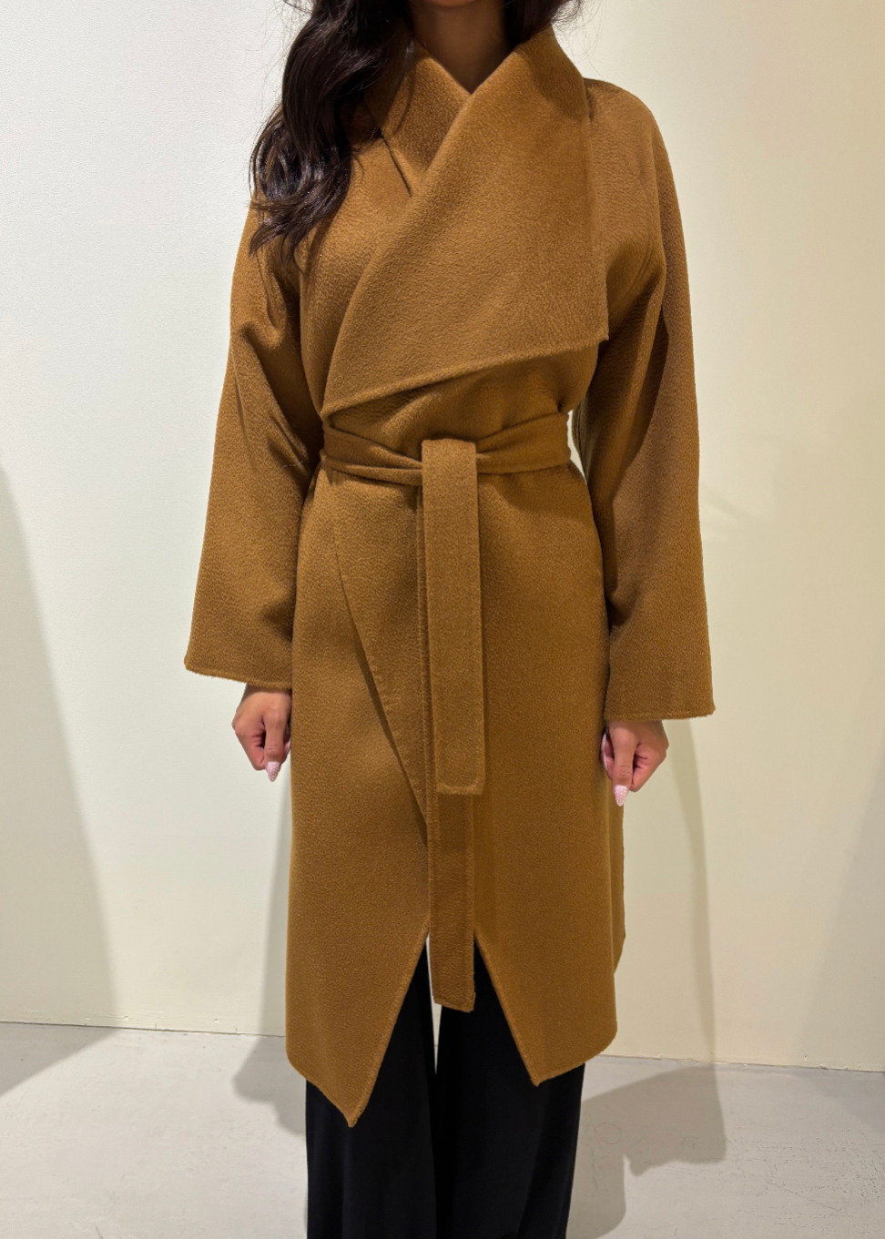Person wearing a brown coat with a belt against a plain background