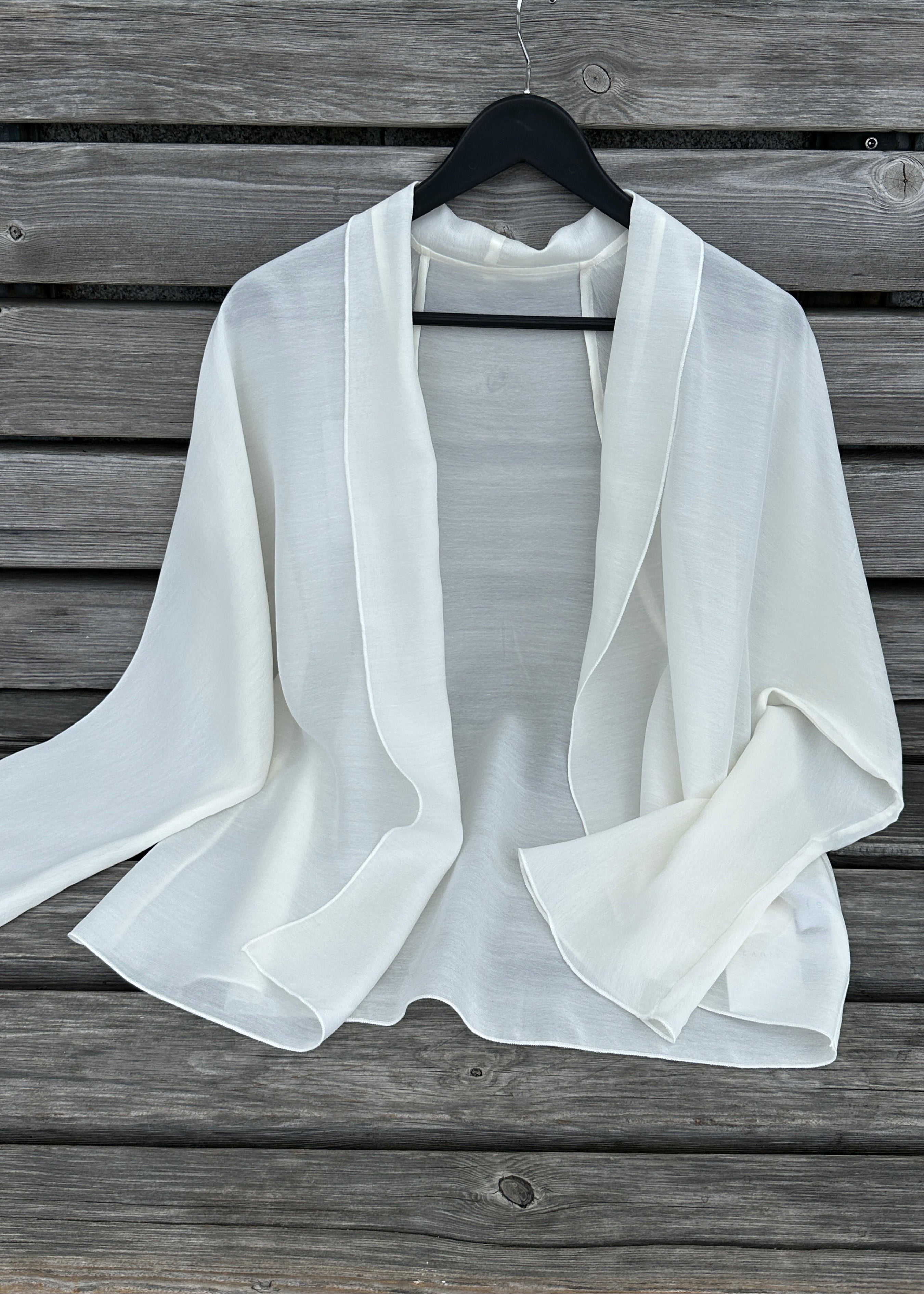 White sheer jacket on a hanger against a wooden background