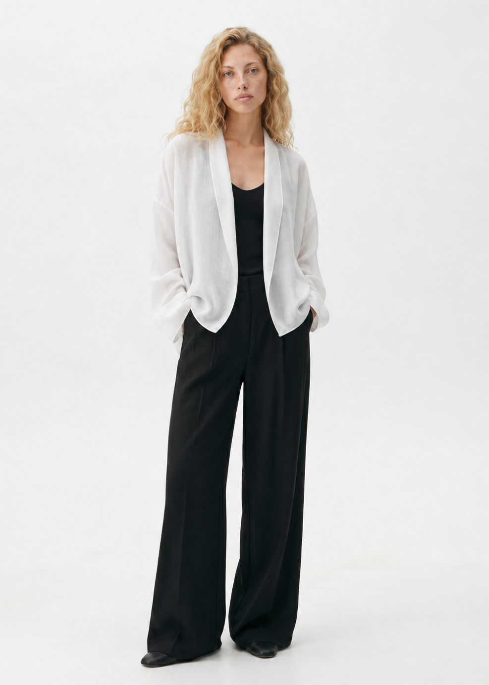 Woman wearing a white blazer and black pants on a white background