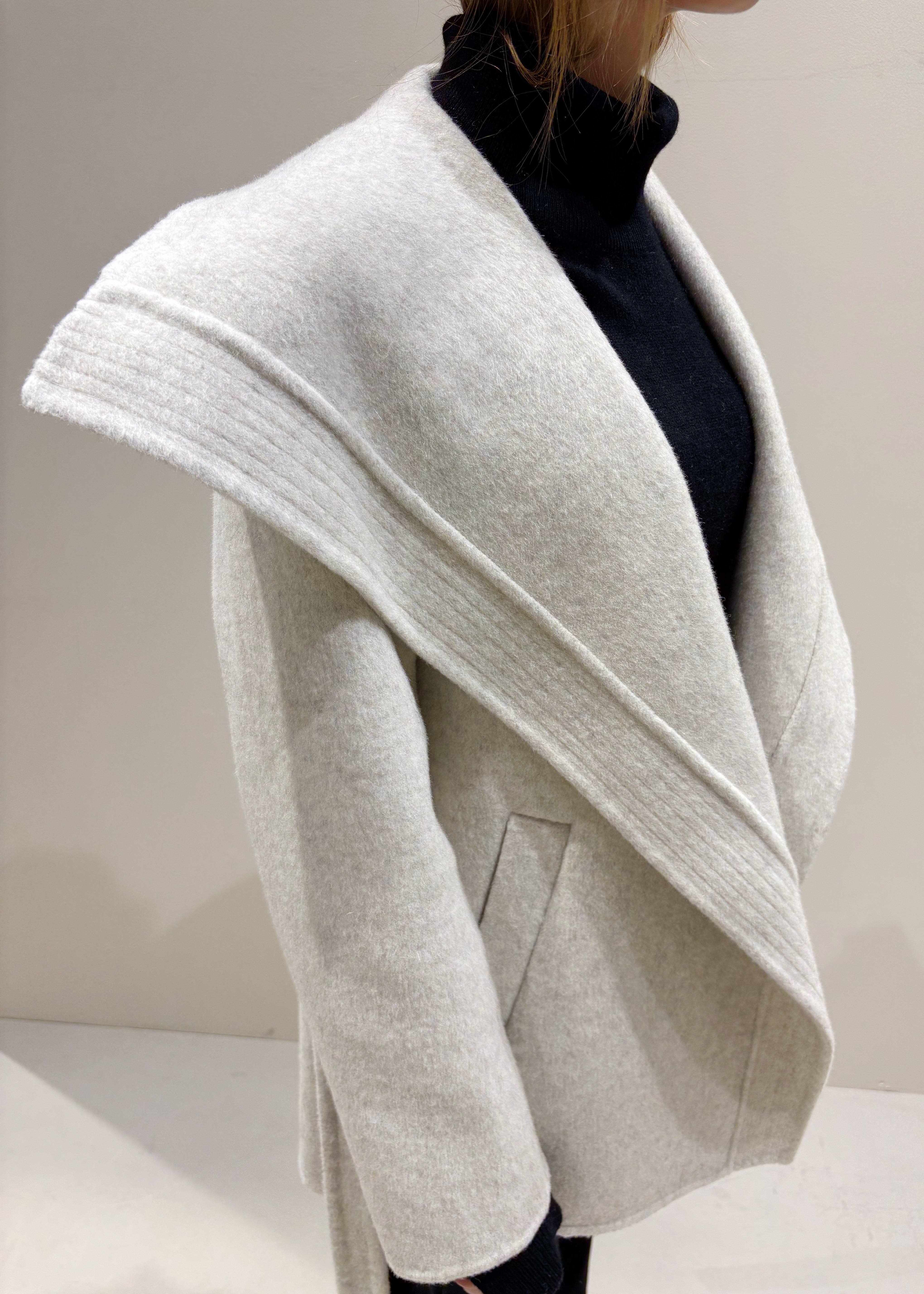 Light gray coat worn by a person on a plain background