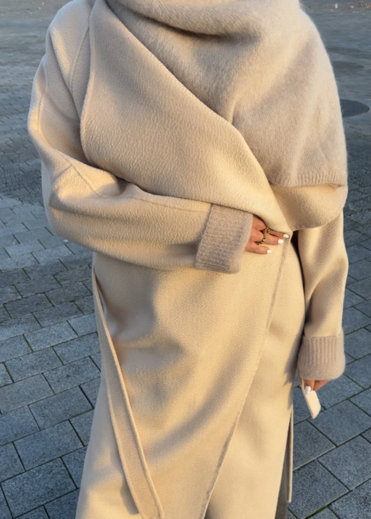 Person wearing a long beige coat on a paved street