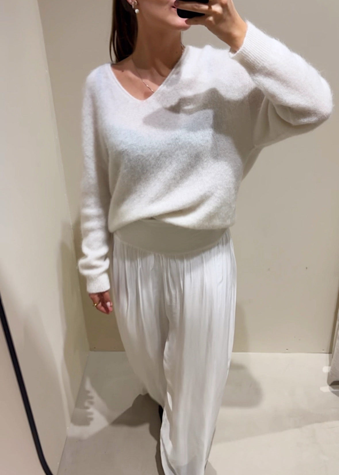 Woman taking a mirror selfie wearing a white sweater and pants.