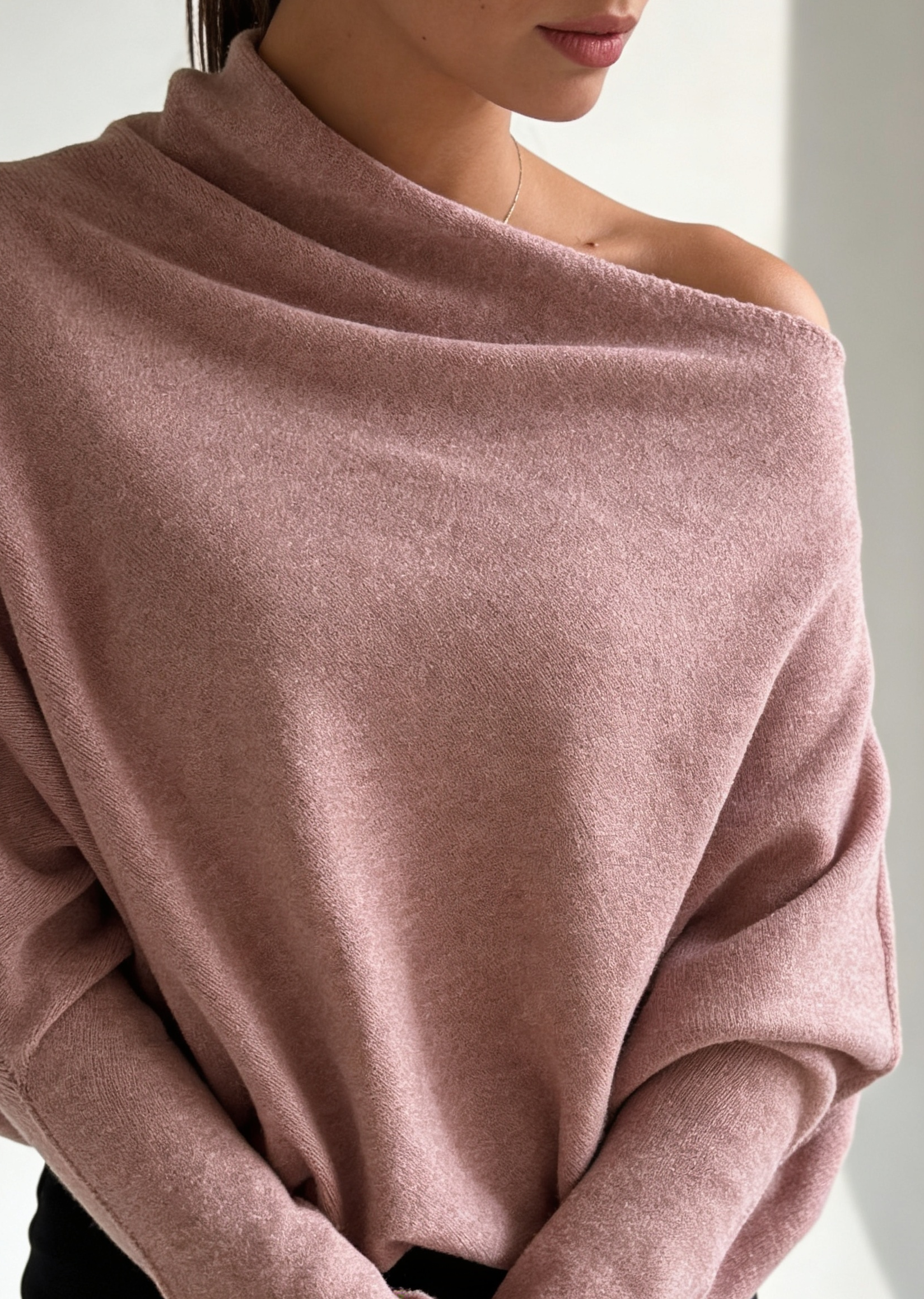 Woman wearing a pink off-shoulder sweater against a white background