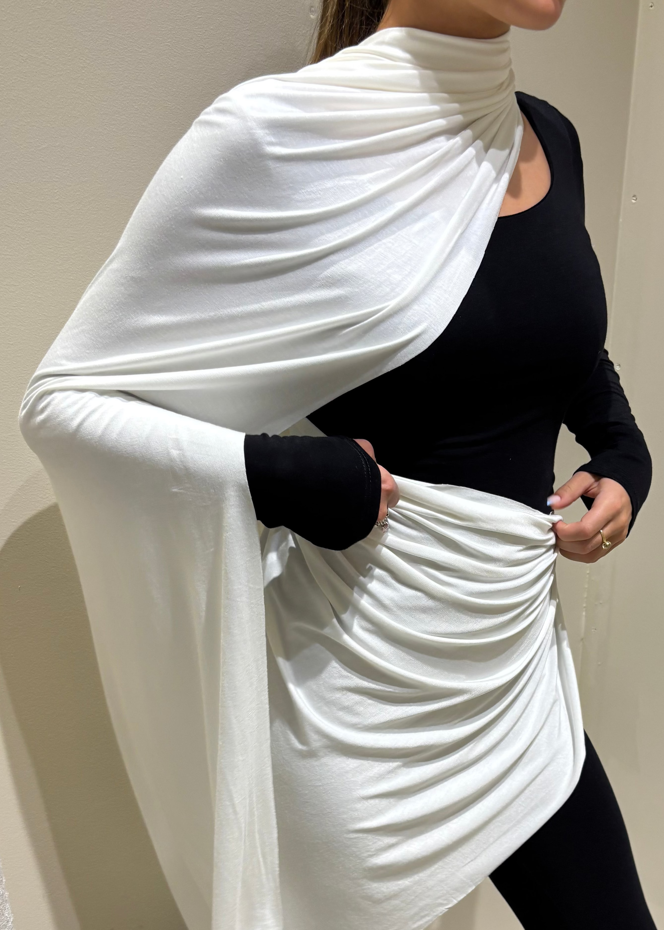 Person wearing a white shawl over a black outfit against a plain background