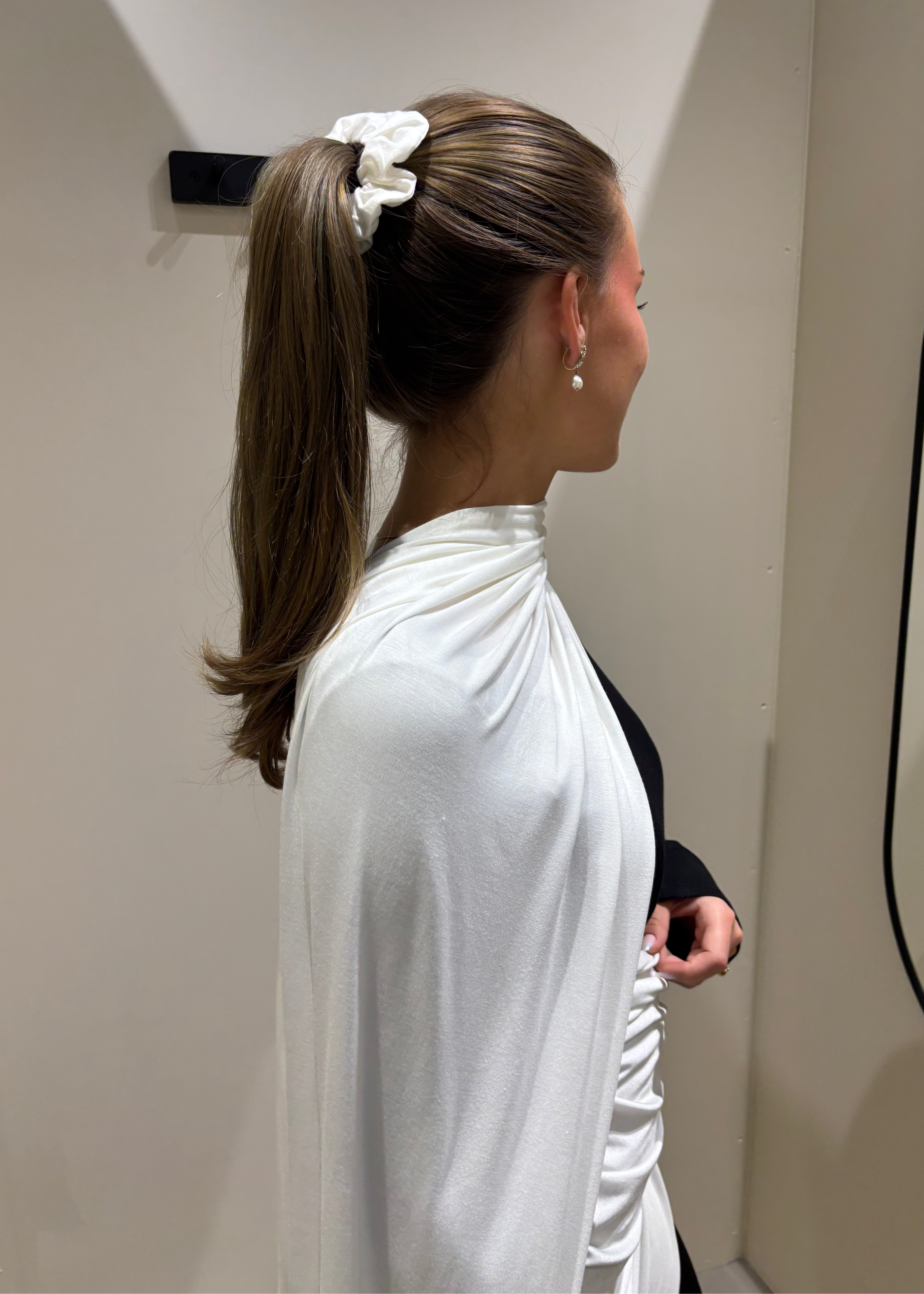 Woman with a ponytail wearing a white top in a neutral setting
