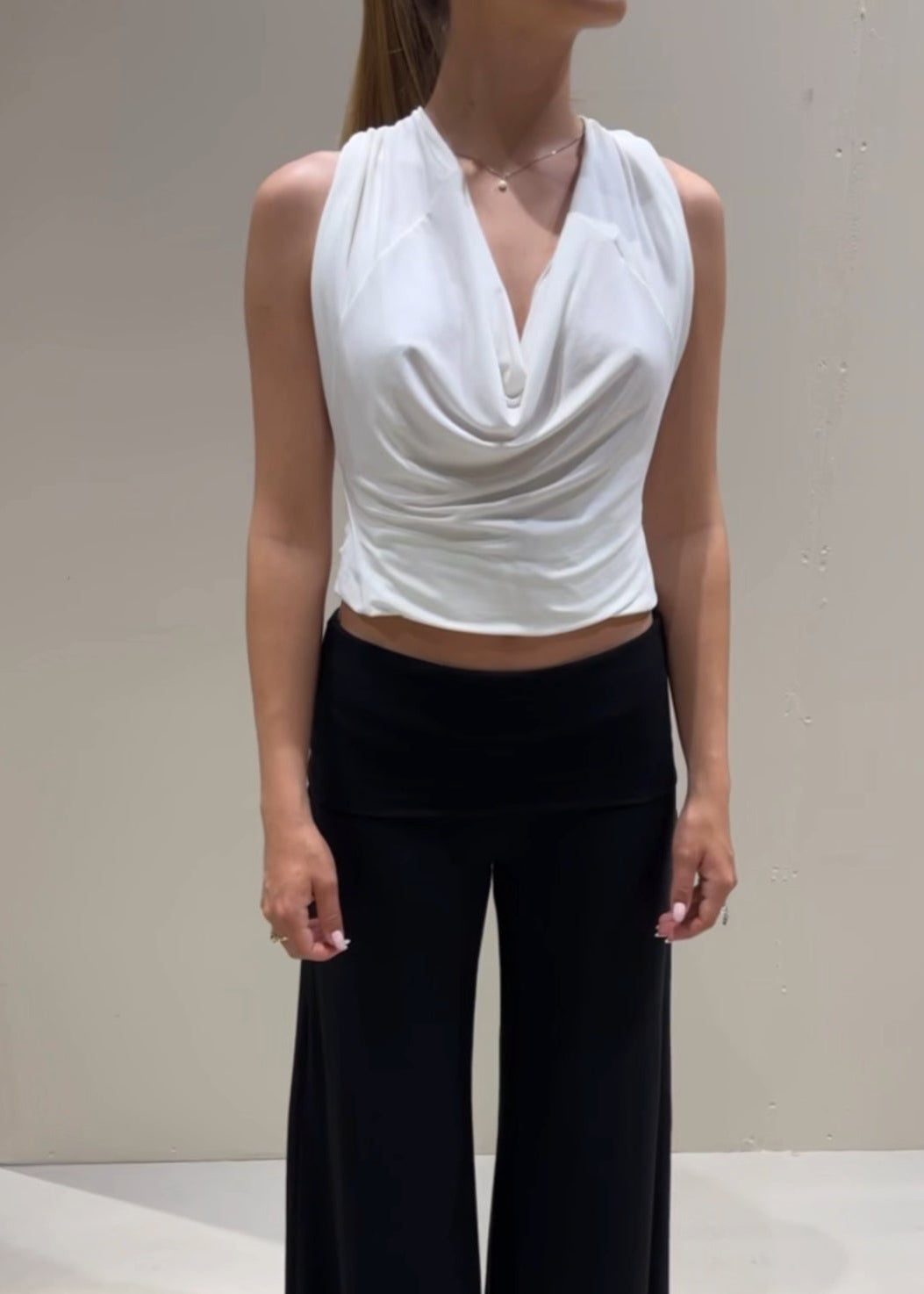 Person wearing a white sleeveless top and black pants against a plain background