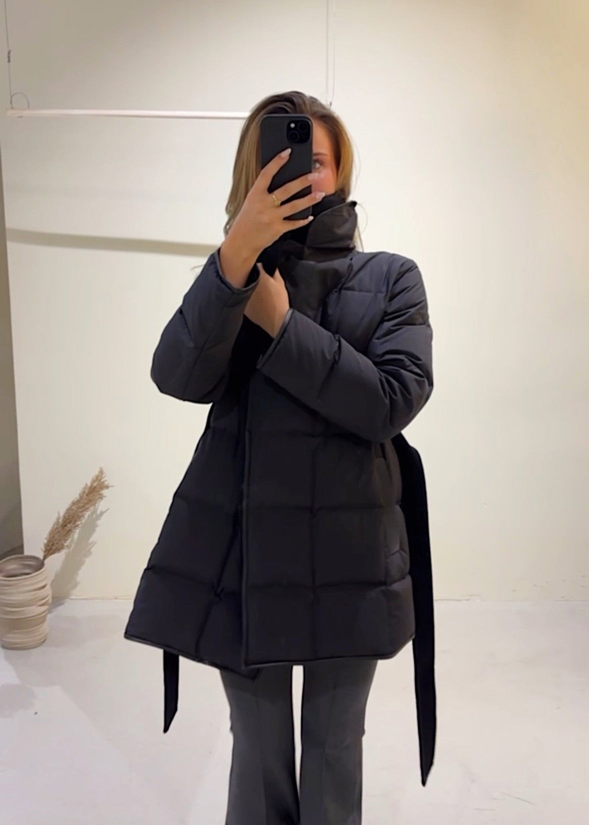 Person wearing a black puffer coat taking a mirror selfie.