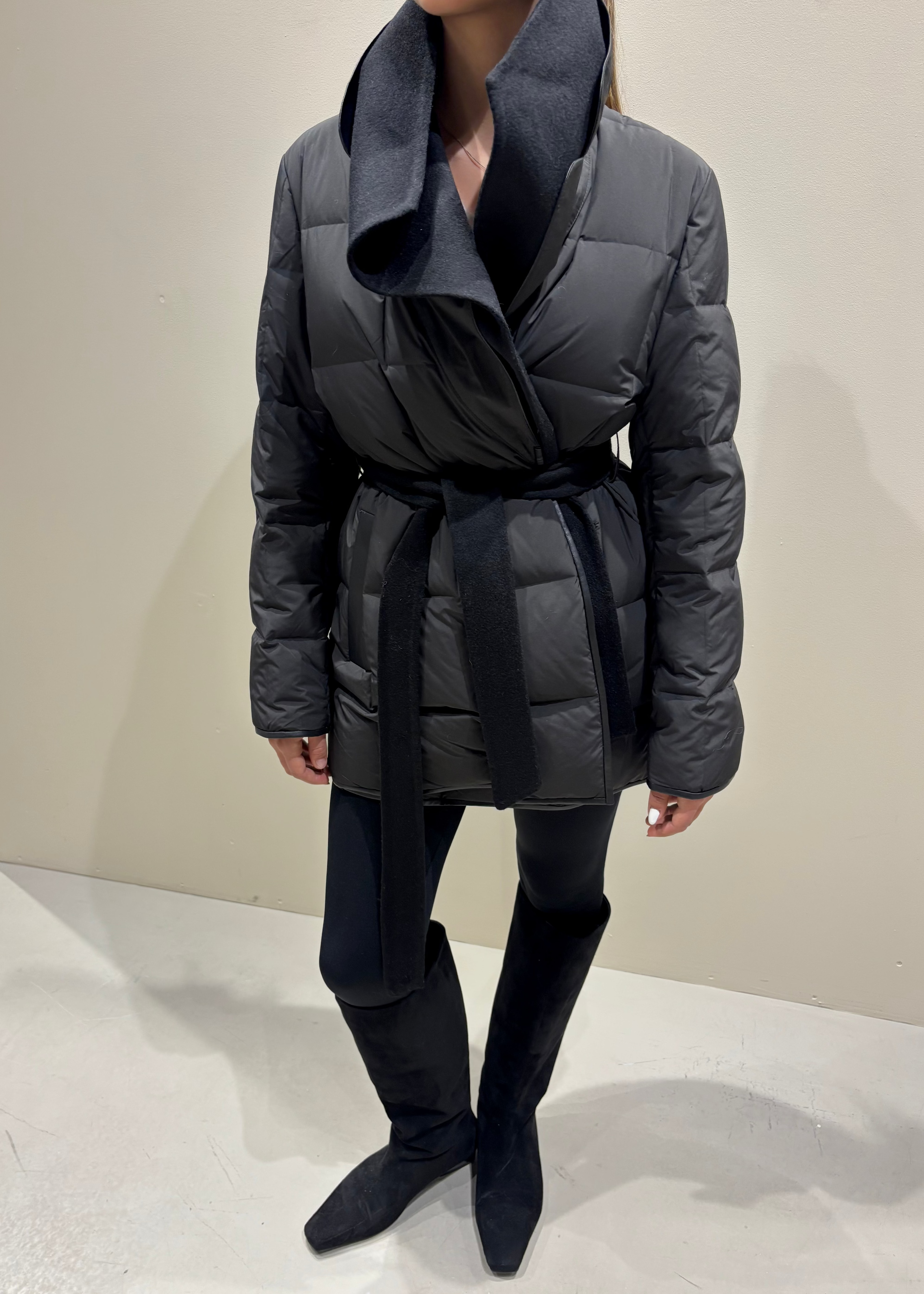 Person wearing a gray puffer coat and black knee-high boots on a plain background