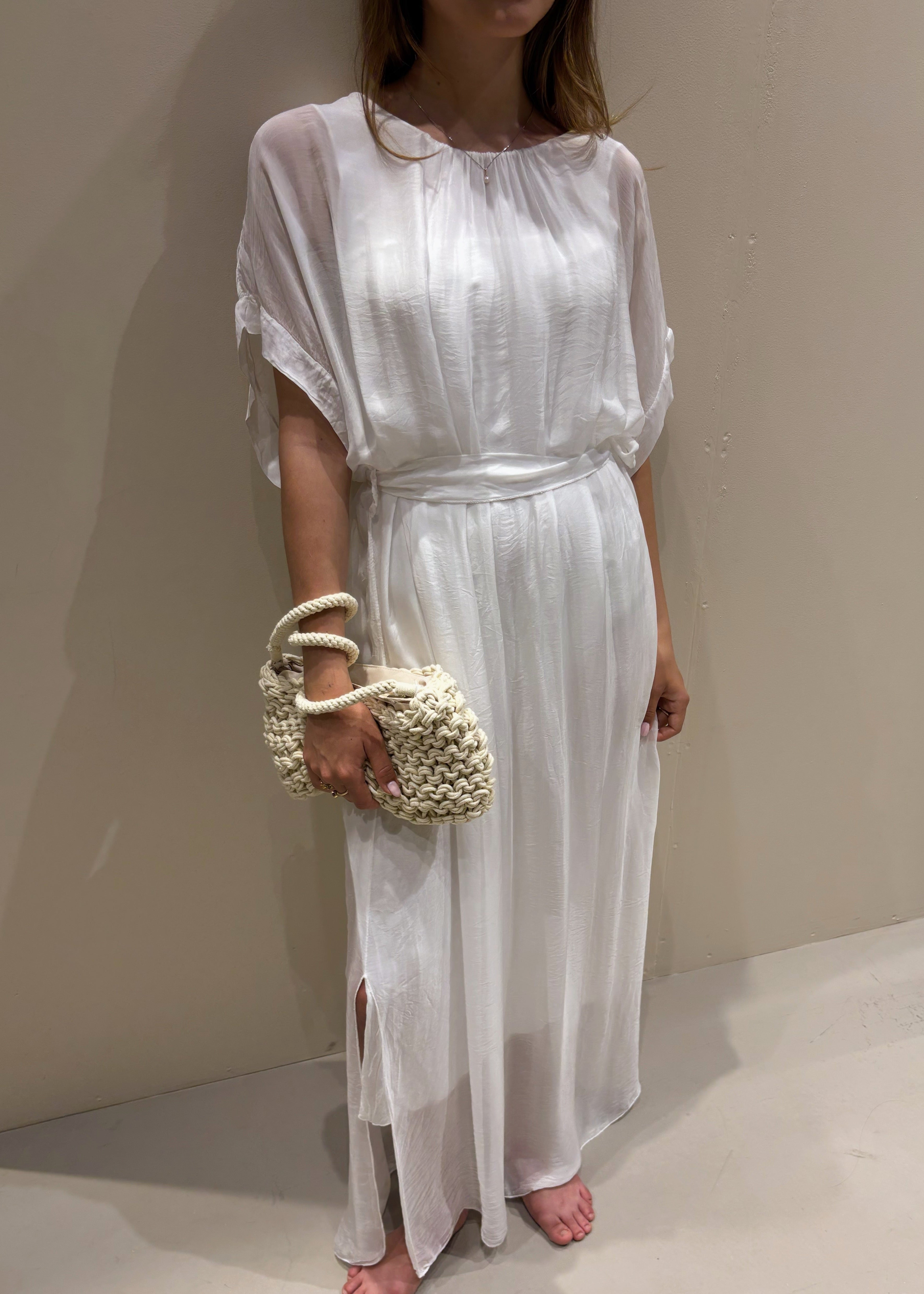 Person wearing a white dress holding a woven handbag against a neutral background