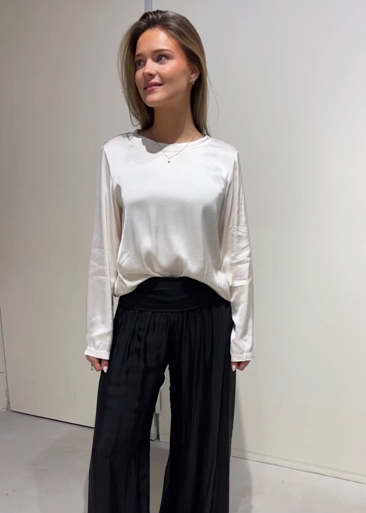 Woman wearing a white blouse and black pants against a plain background