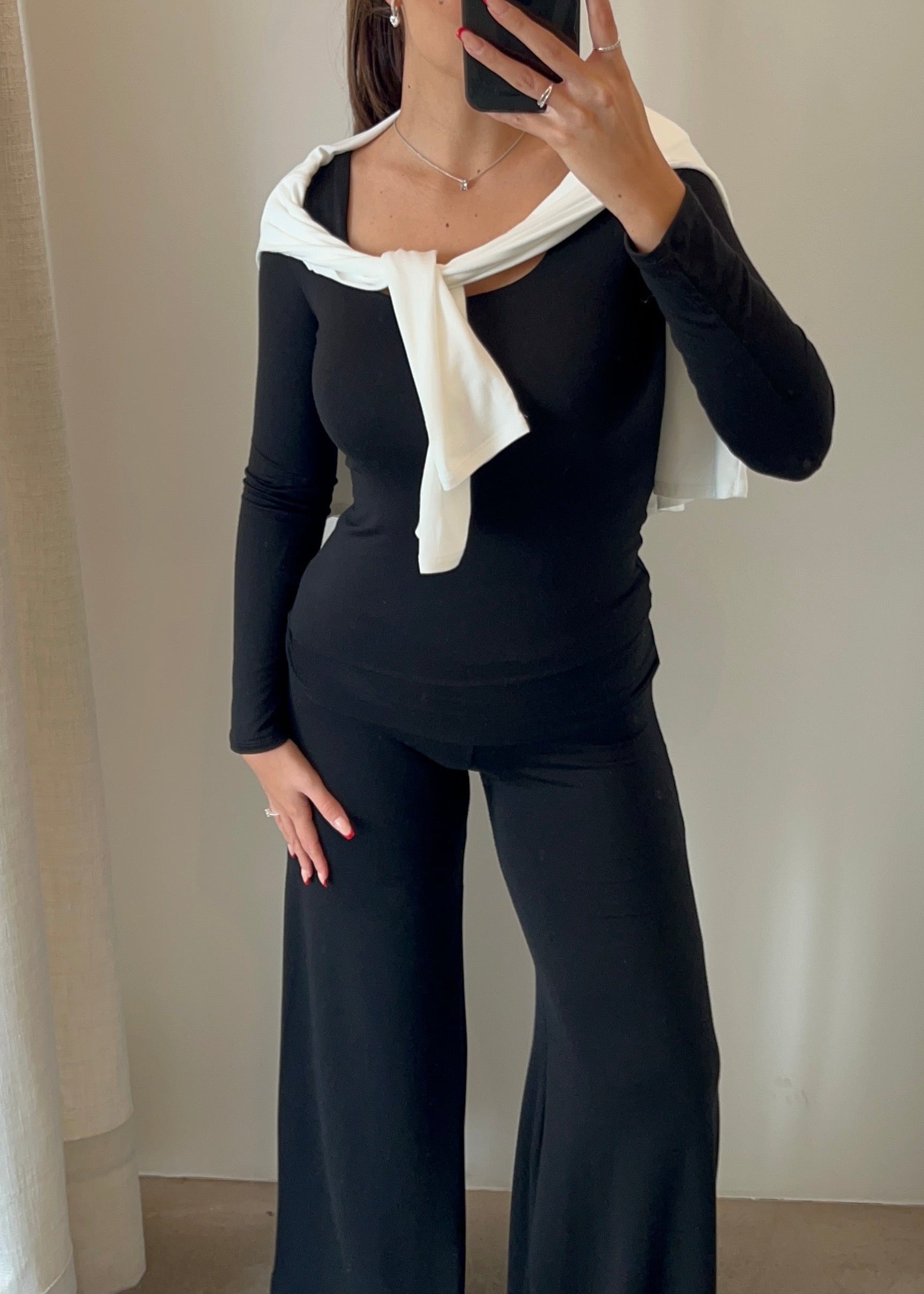 Person wearing a black outfit with a white bow tie in front of a neutral background