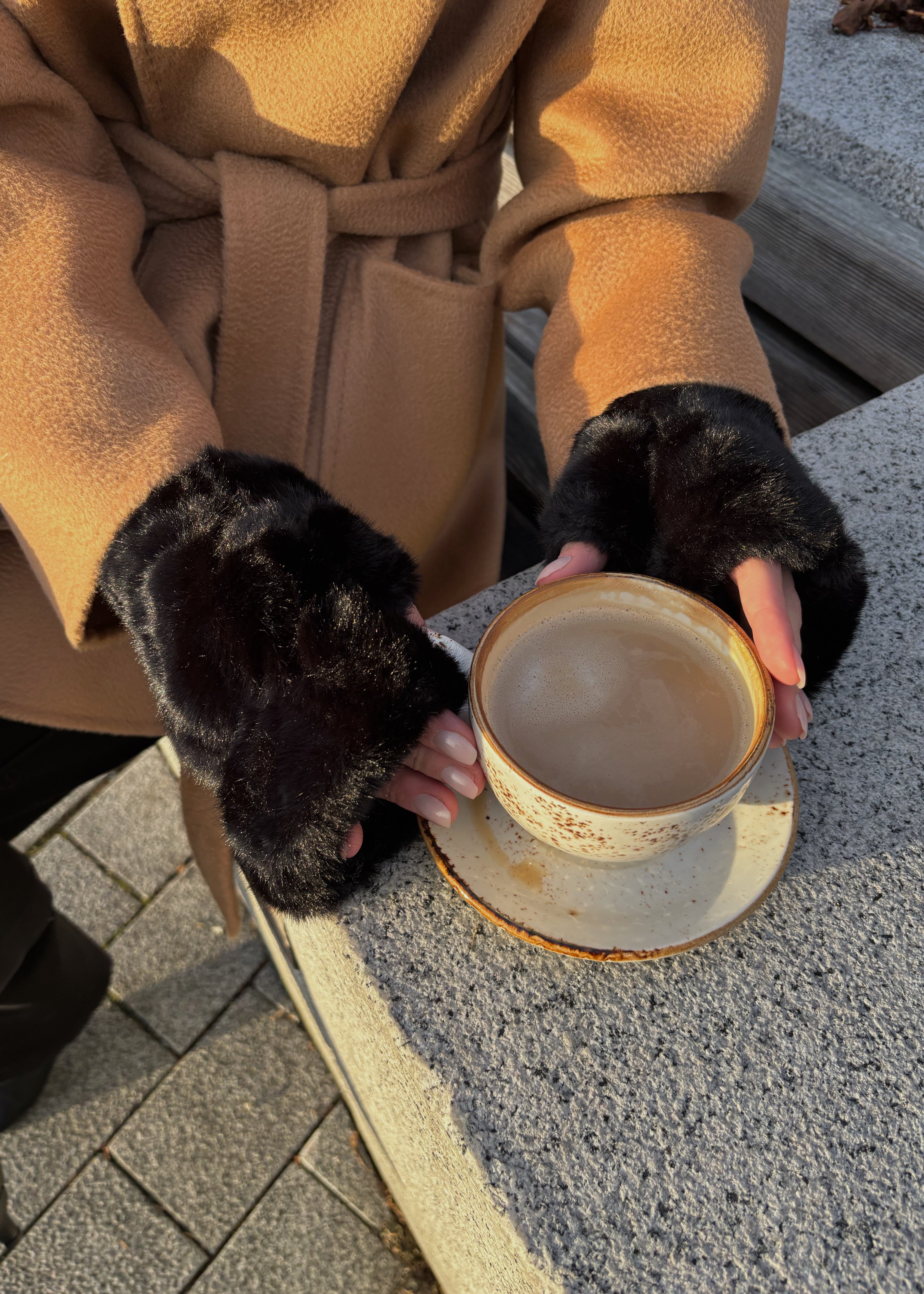 Person in a brown coat and black gloves holding a cup outdoors.