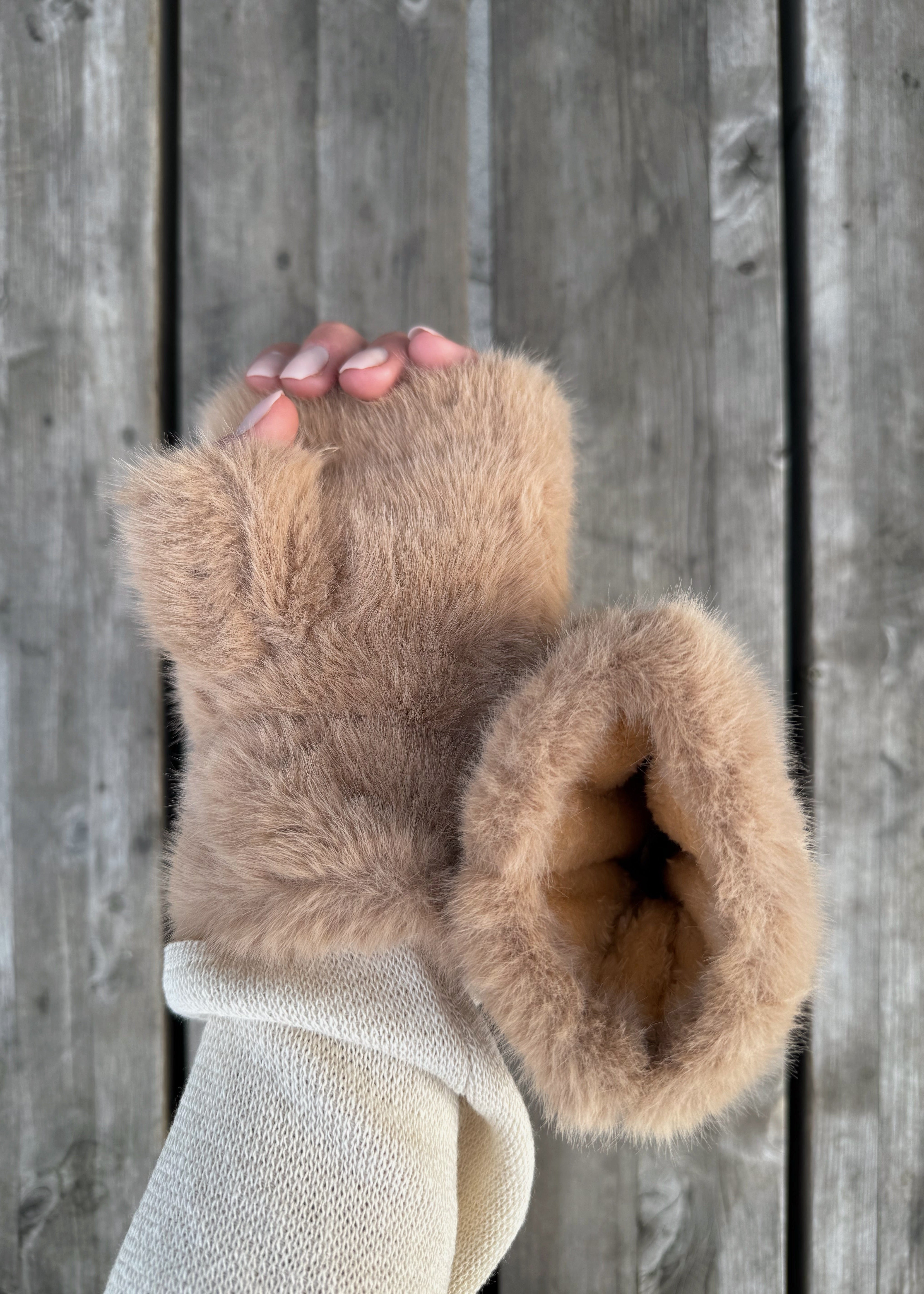 Brown fuzzy gloves held against a wooden background
