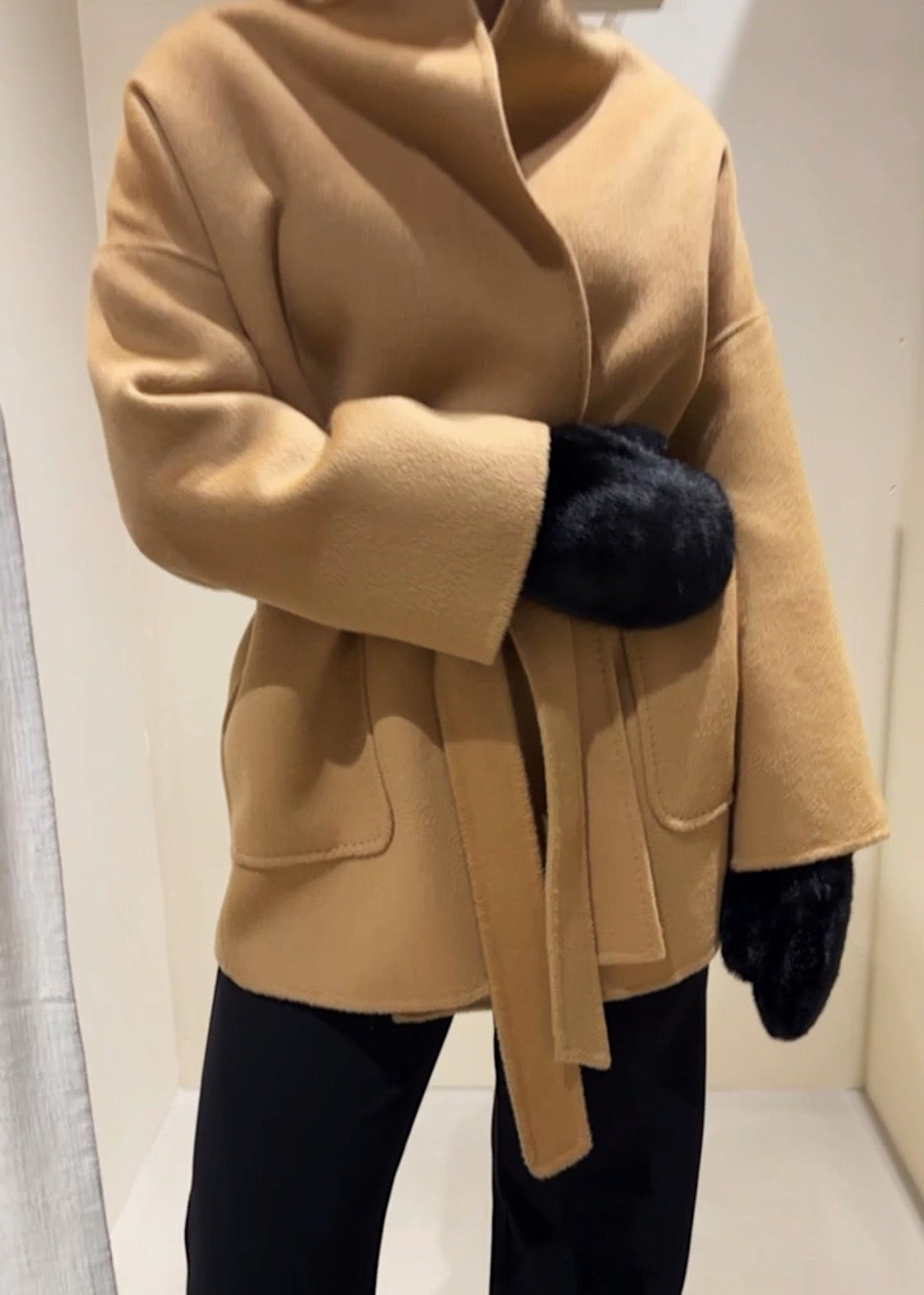 Beige coat with a belt and black gloves on a neutral background