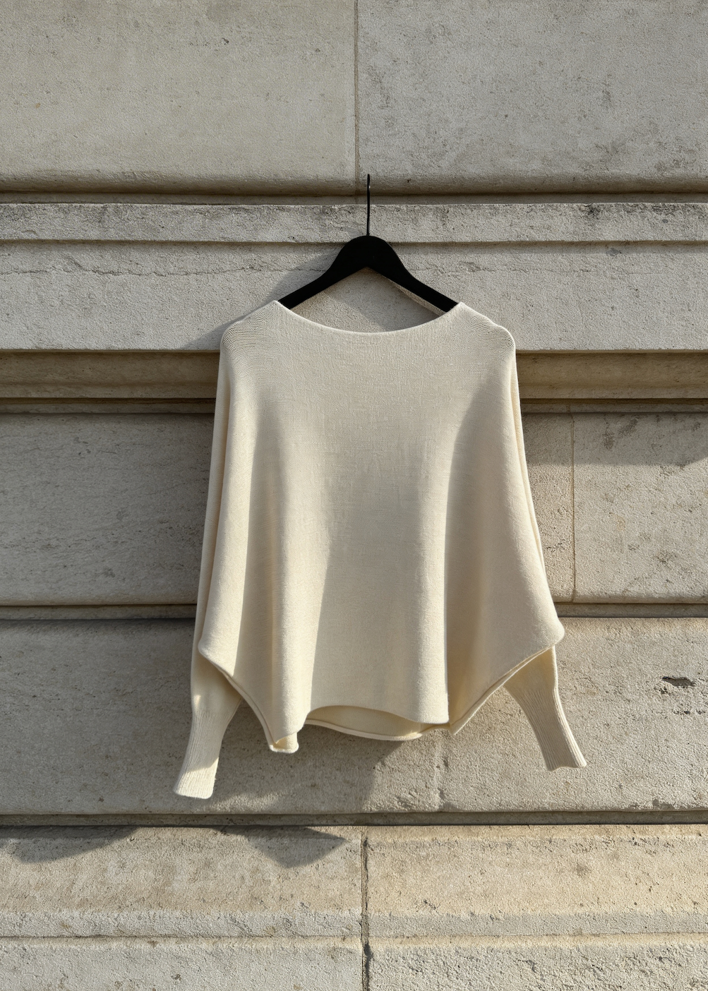 Beige sweater on a hanger against a stone wall