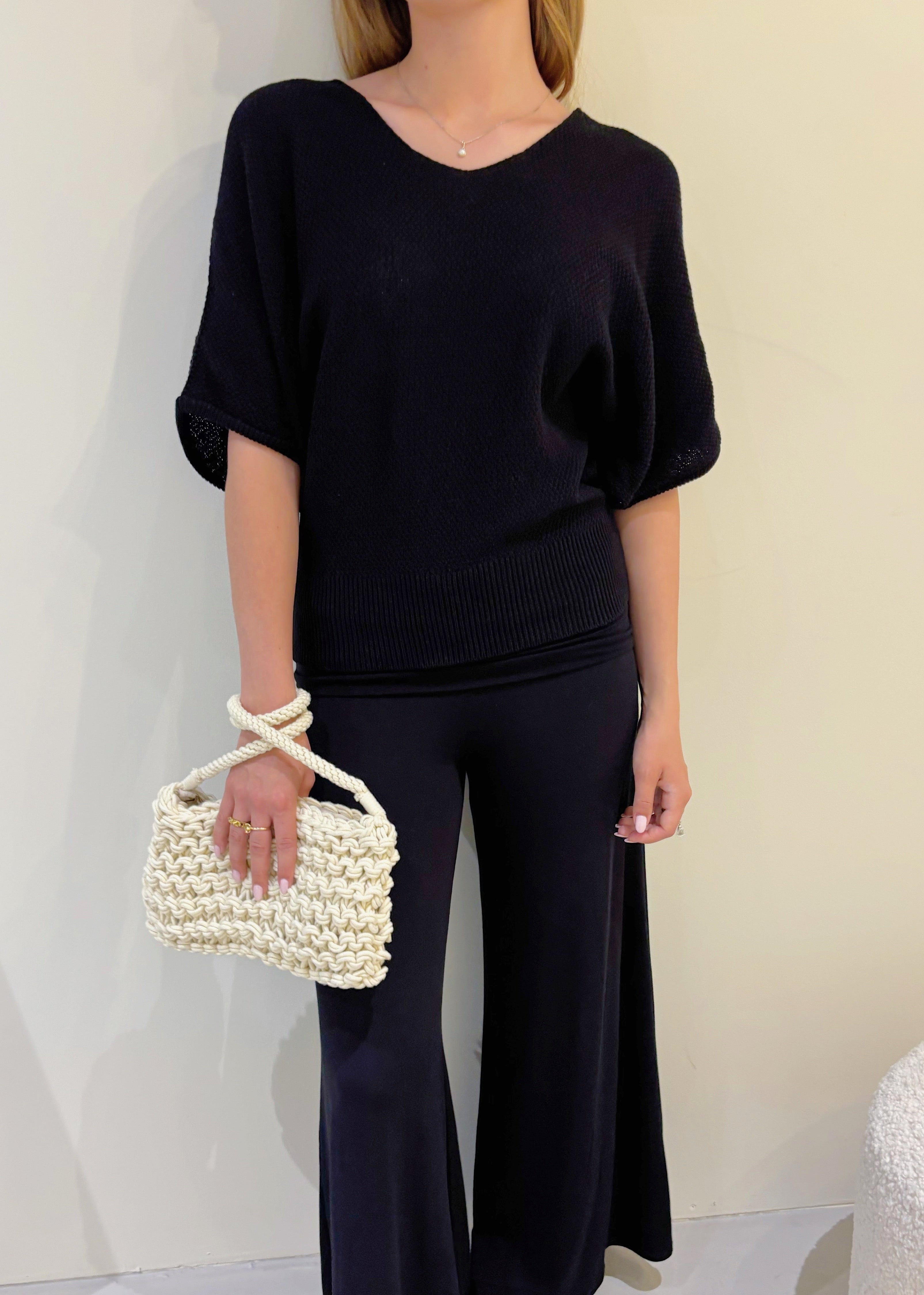 Person wearing a black outfit with a pearl-handled bag against a neutral background