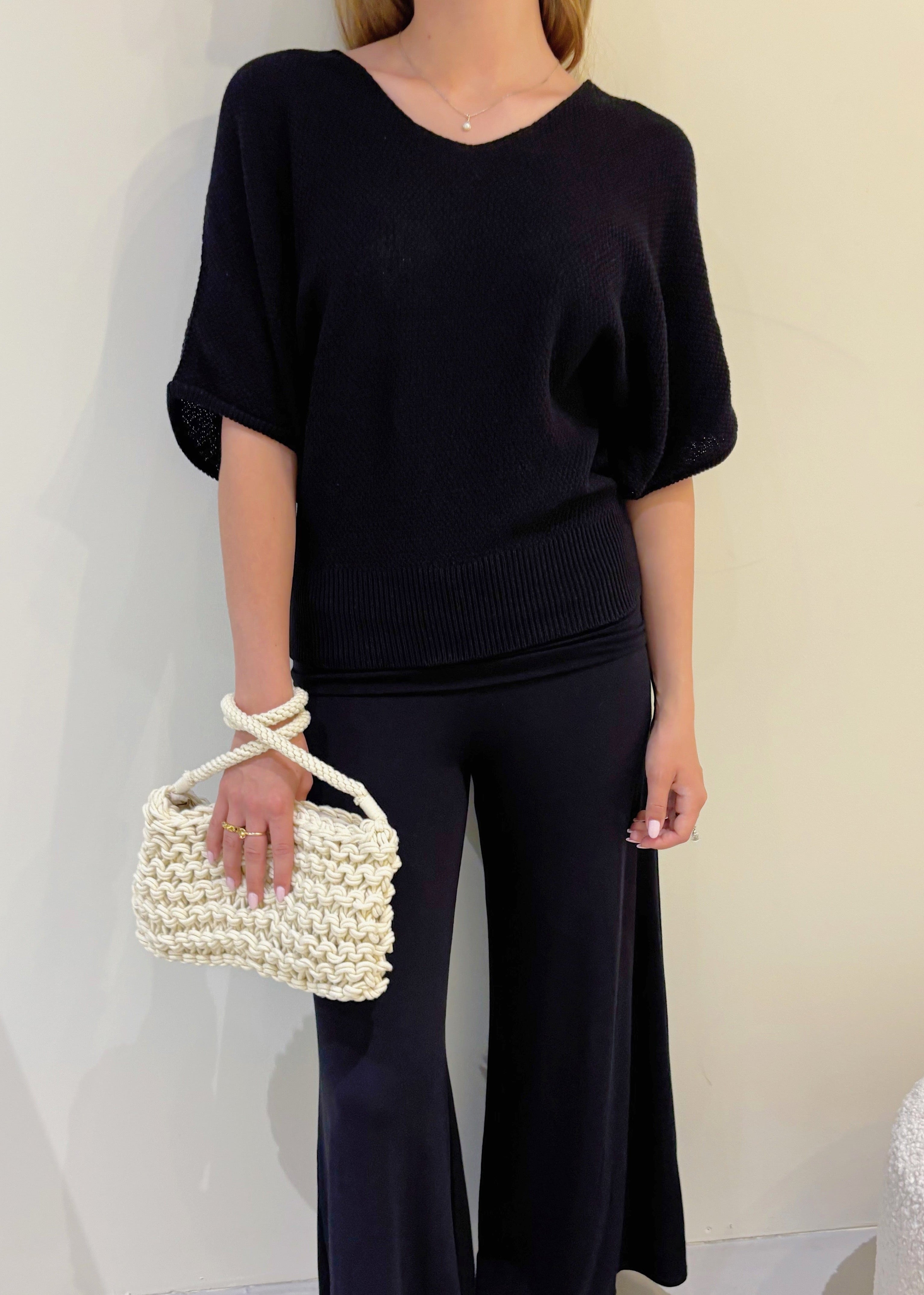 Person wearing a black outfit with a pearl-handled bag against a neutral background
