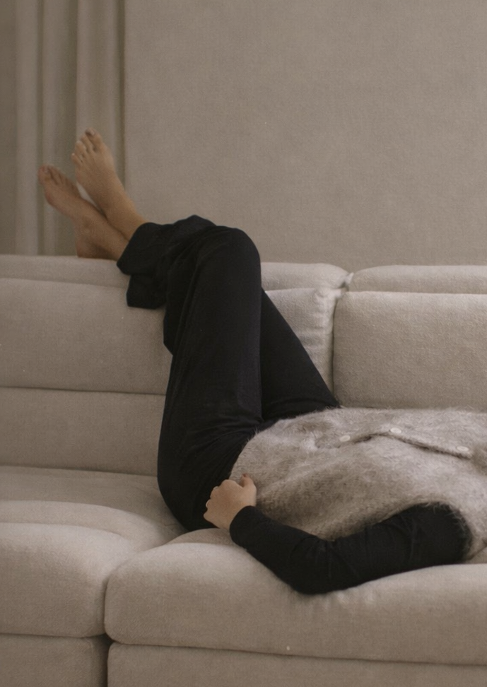 Woman lying on a beige sofa with a newspaper on a table in front of her.