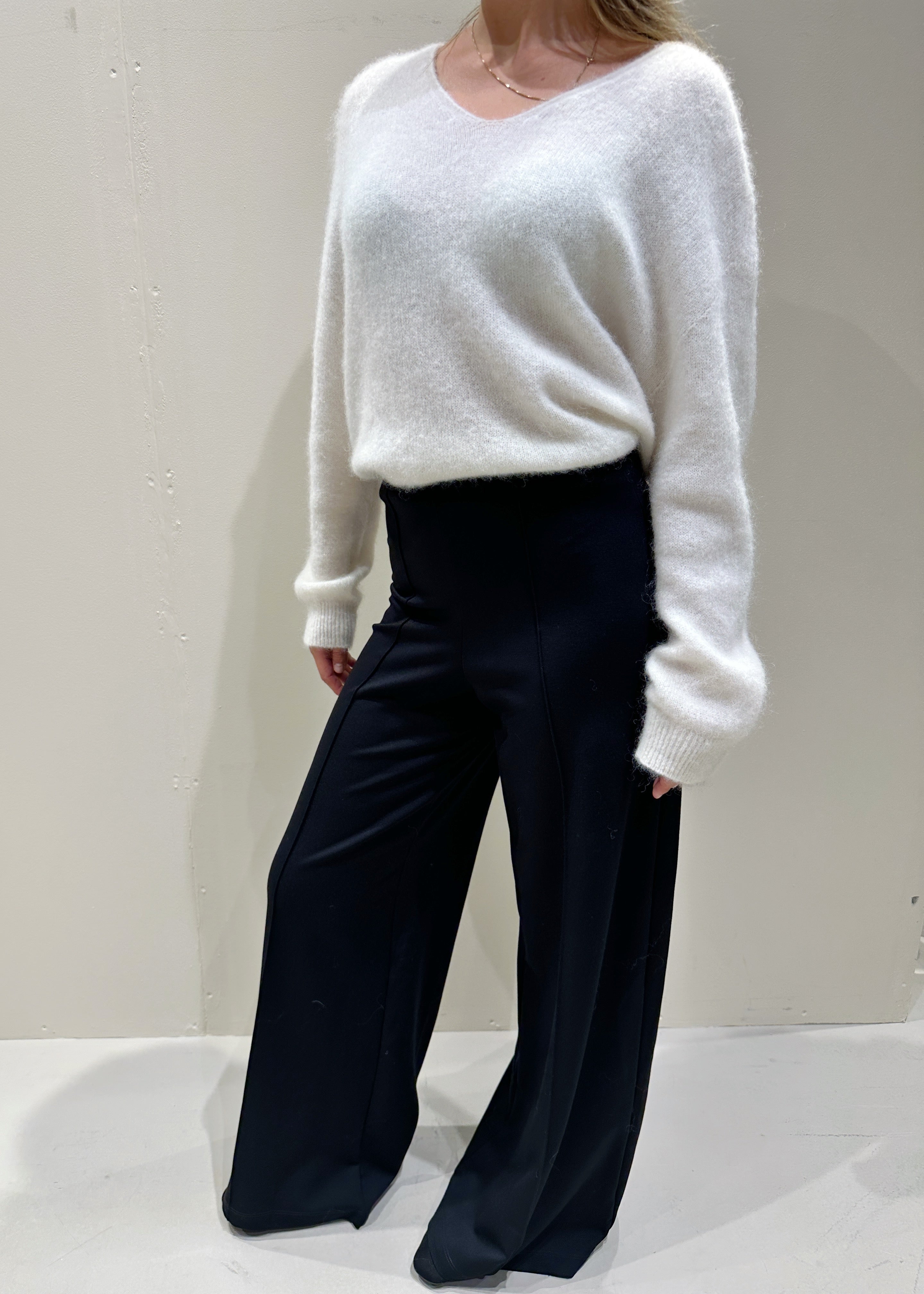 Person wearing a white sweater and black pants on a plain background