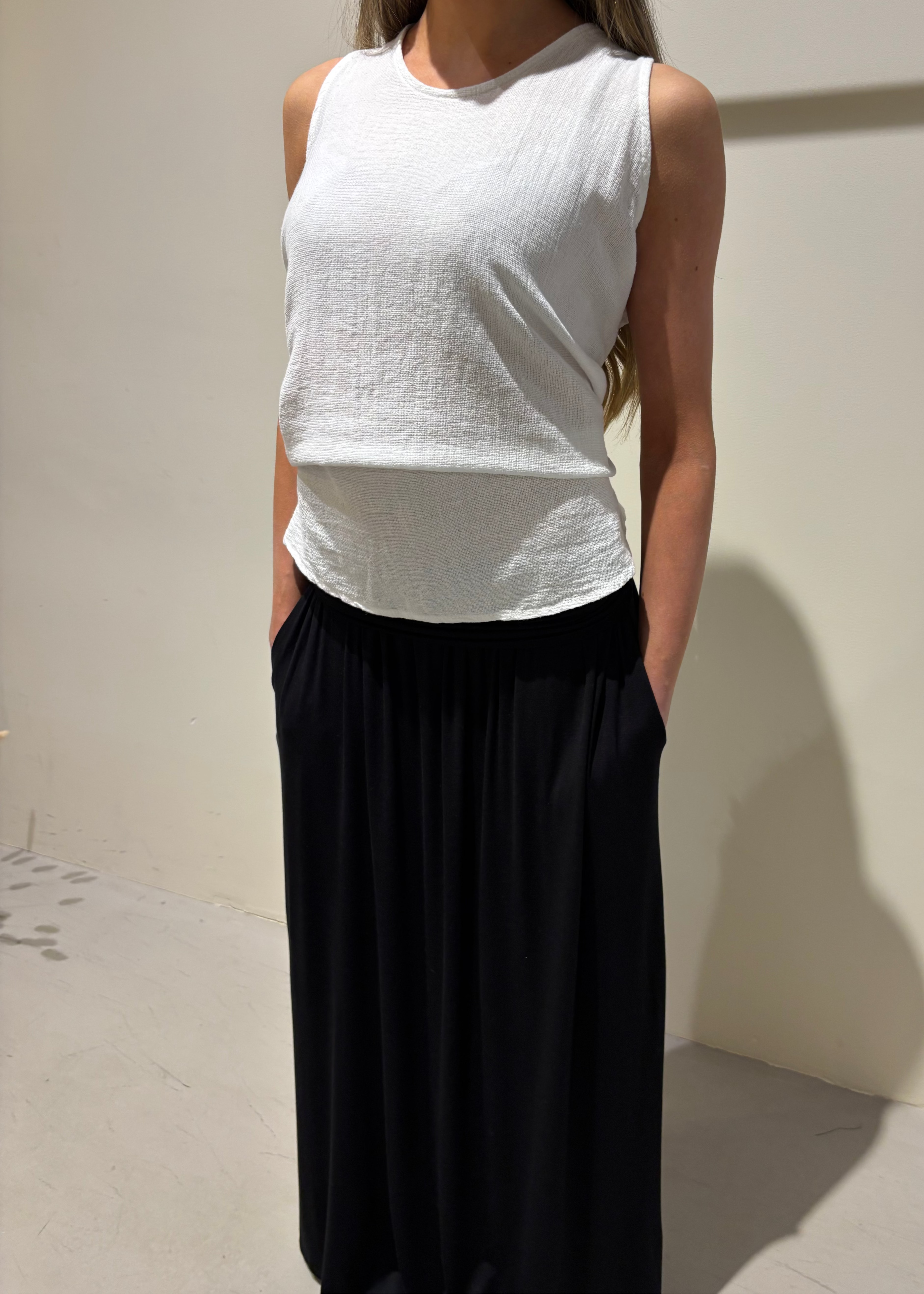 Person wearing a white sleeveless top and black pants against a plain background