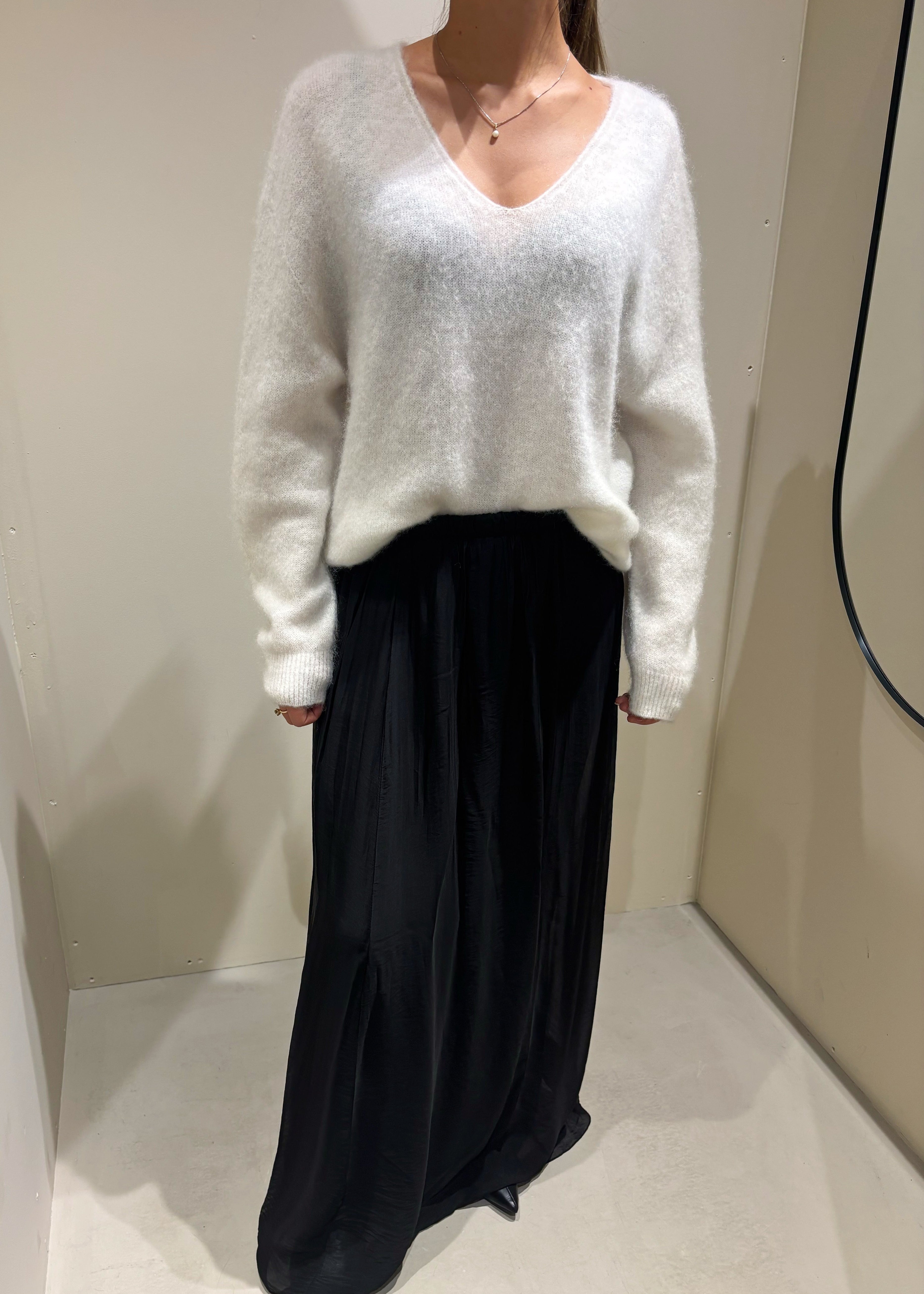 Person wearing a white sweater and black skirt in a neutral setting