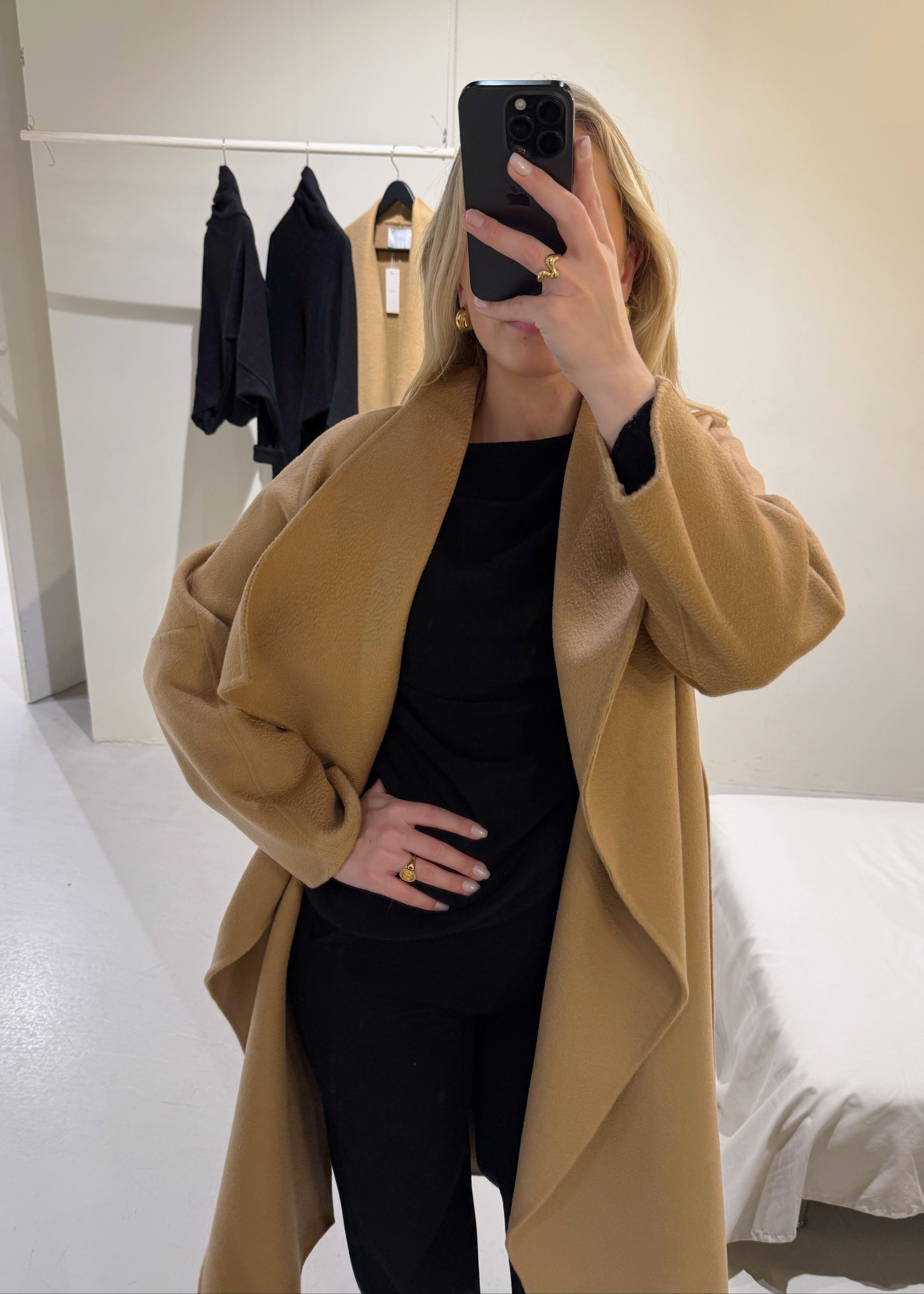 Person wearing a beige coat taking a mirror selfie in a room.