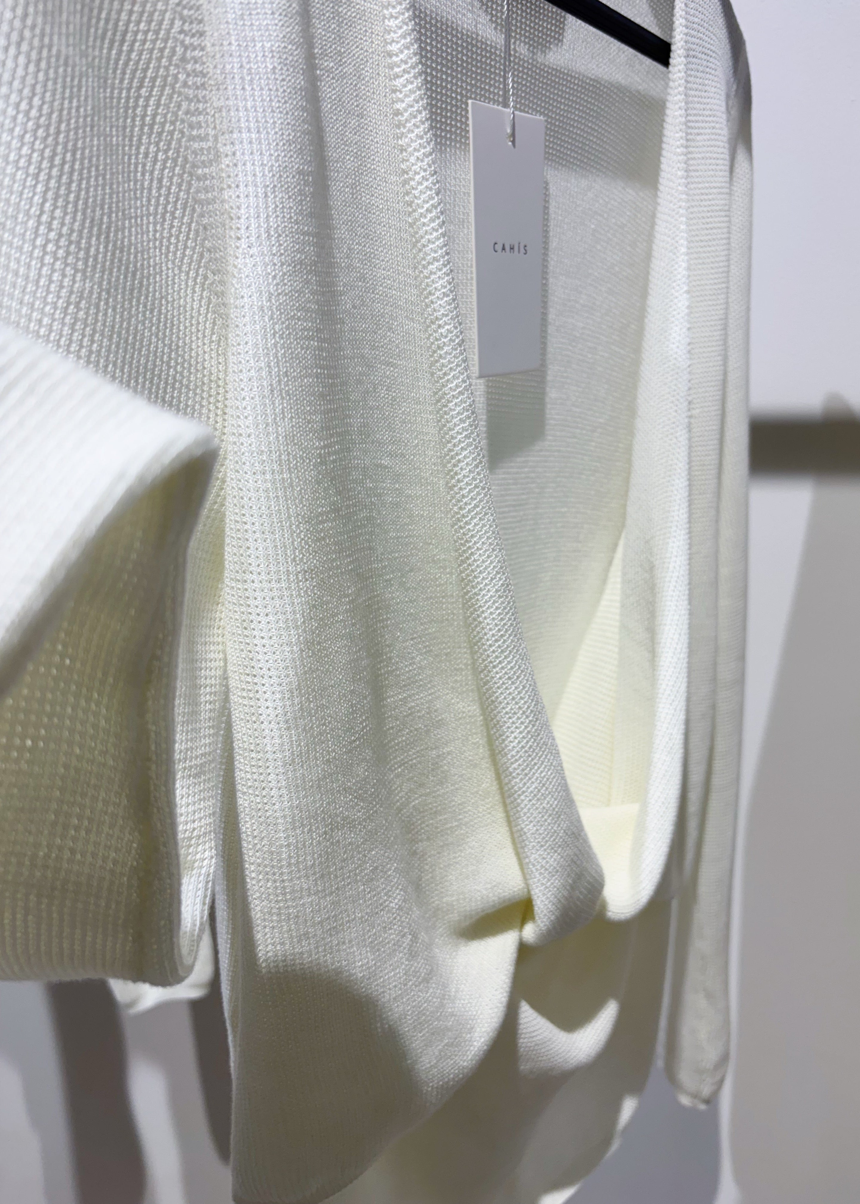 White knit cardigan on a rack with a visible brand tag.