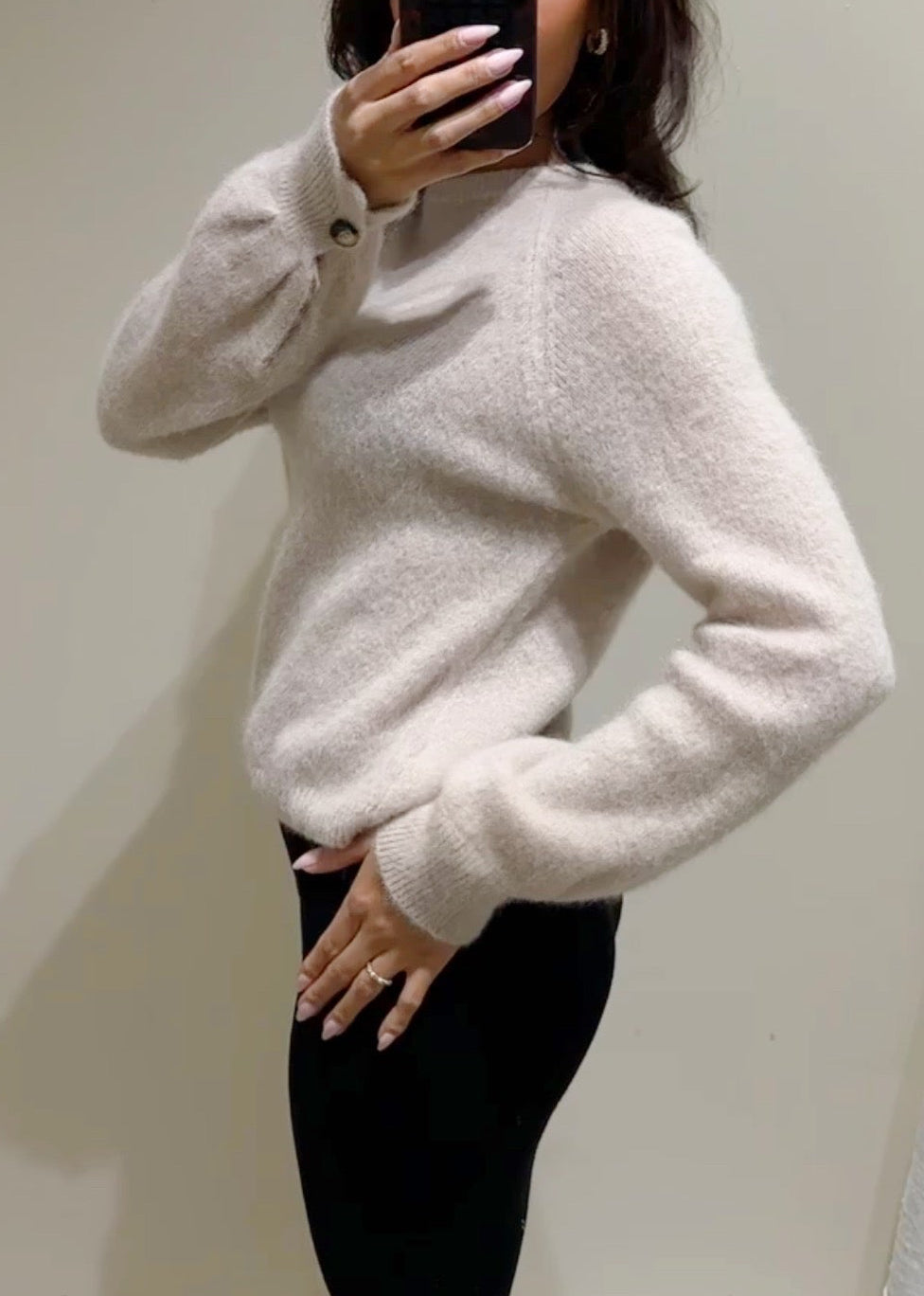 Person wearing a sand sweater taking a mirror selfie.