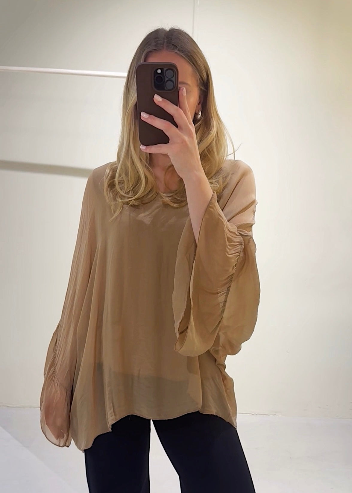 Person wearing a beige blouse taking a mirror selfie.