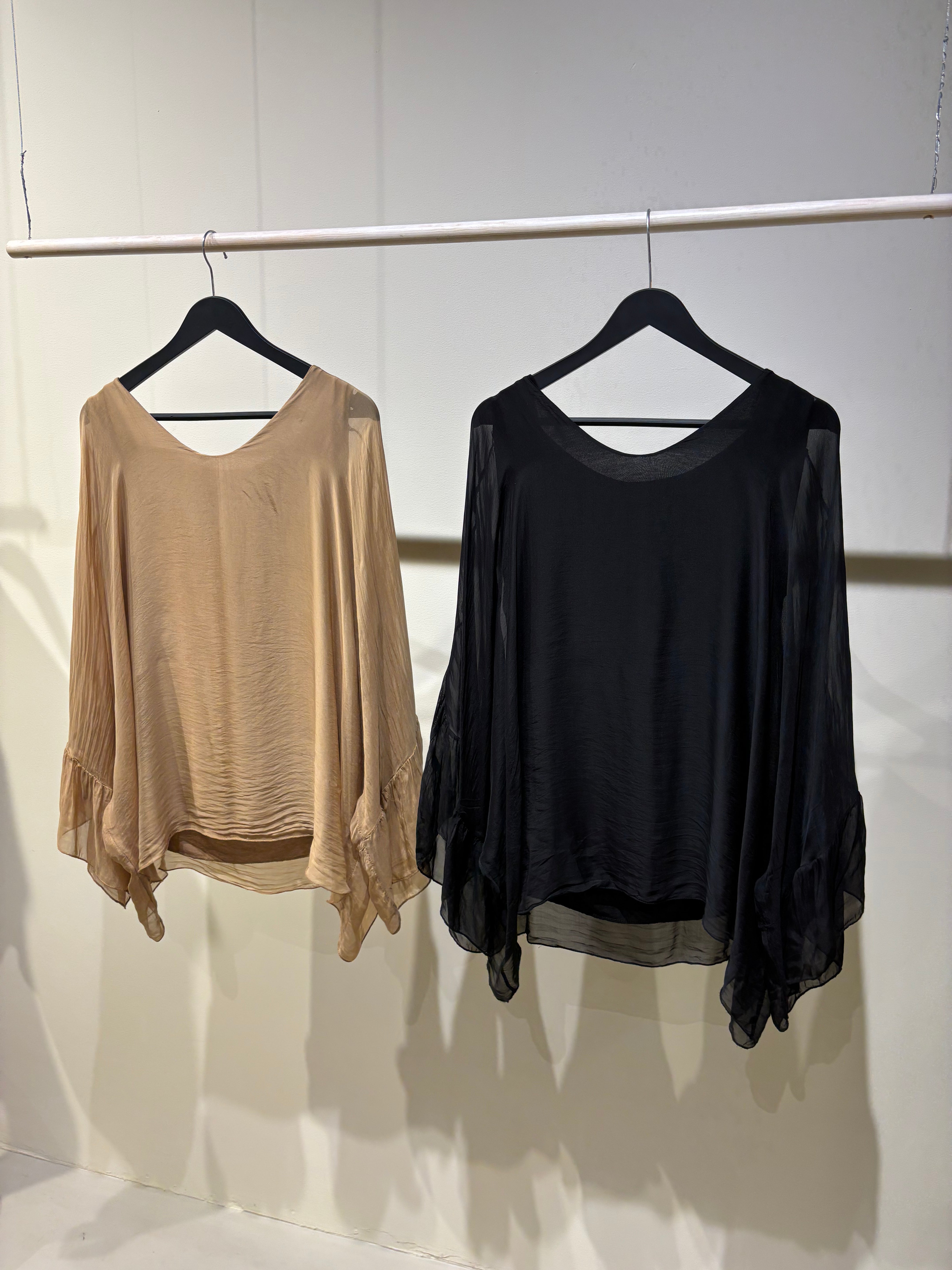 Two shirts, one beige and one black, hanging on a rack against a white wall.