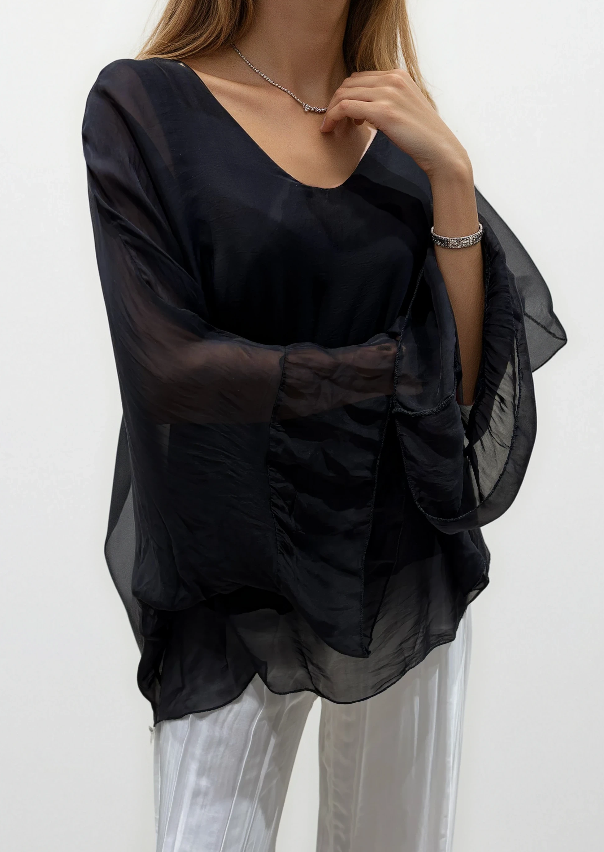 Woman wearing a black sheer top and white pants on a white background