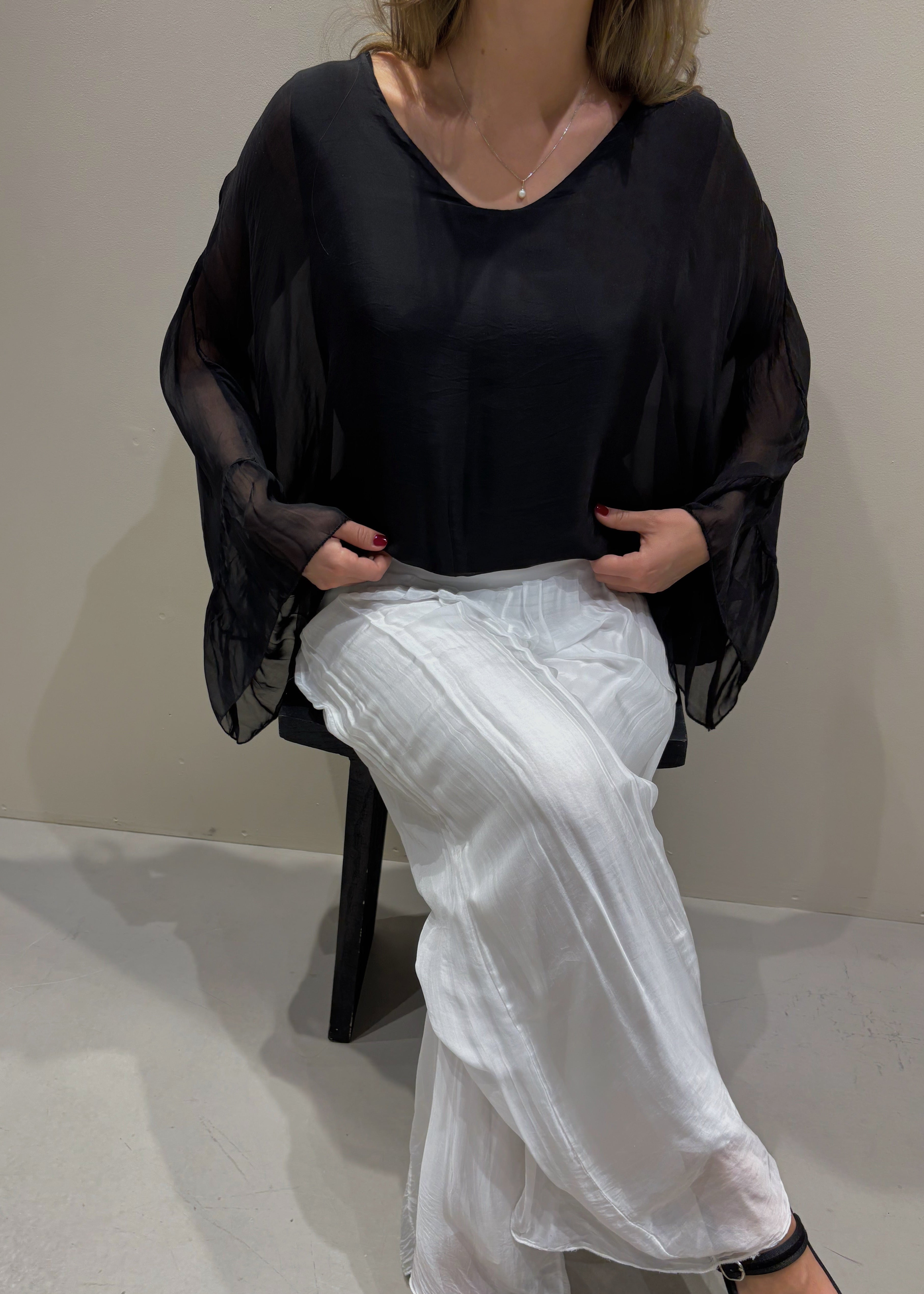 Person wearing a black top and white pants sitting on a chair against a plain background