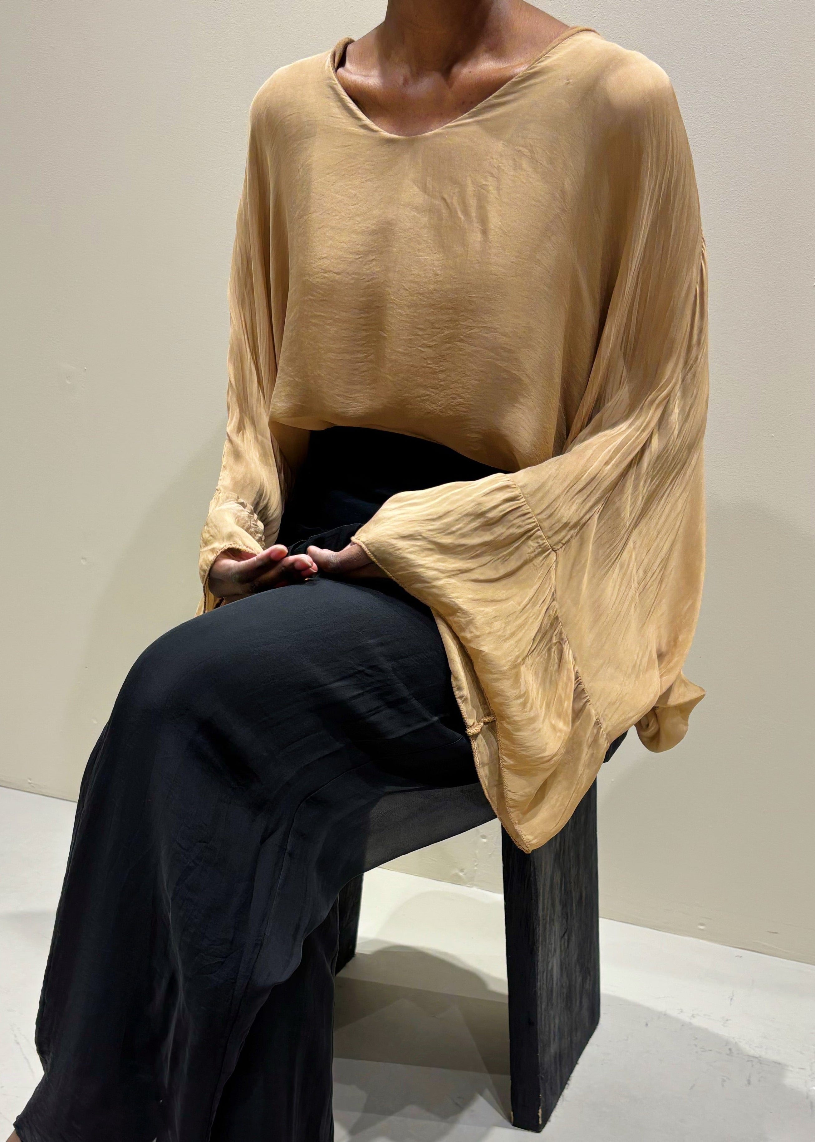 Person wearing a beige sweater and black pants sitting on a chair.