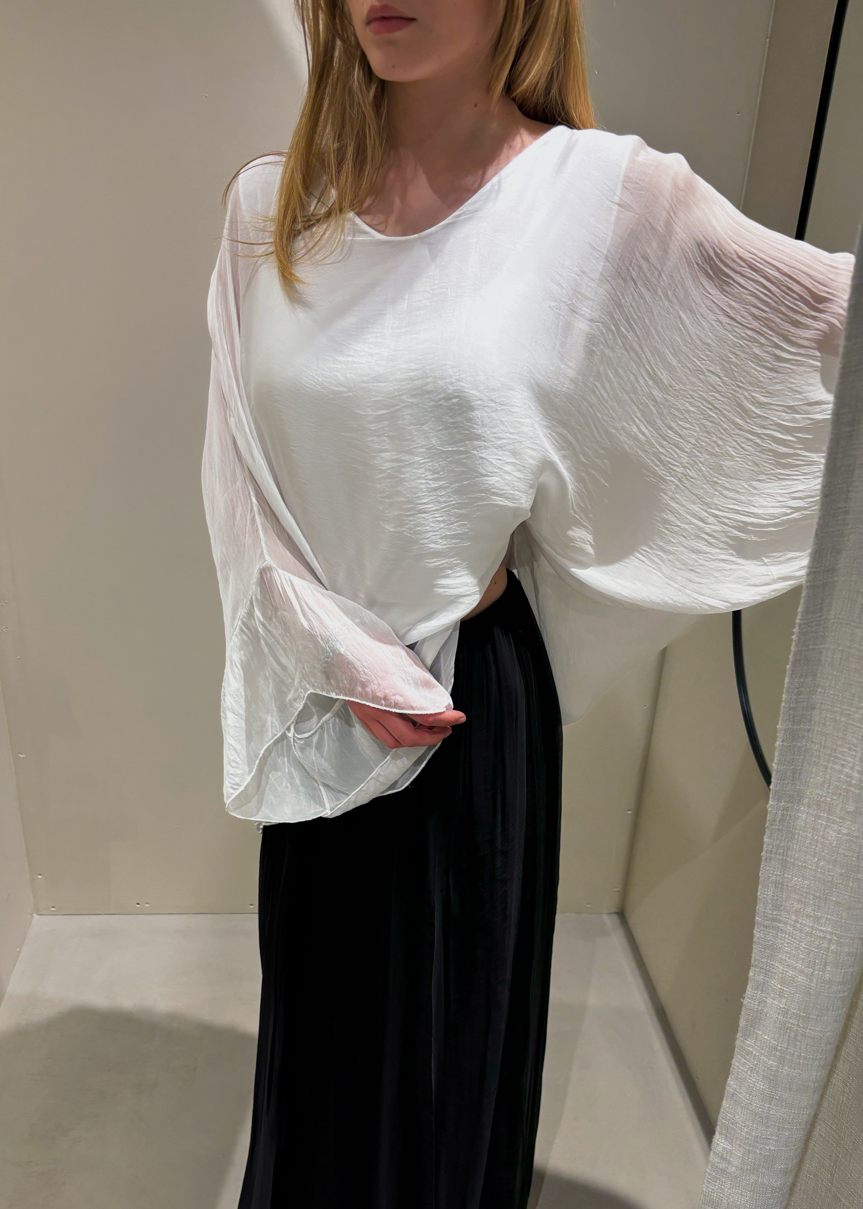 Person wearing a white blouse and black pants in a minimal indoor setting