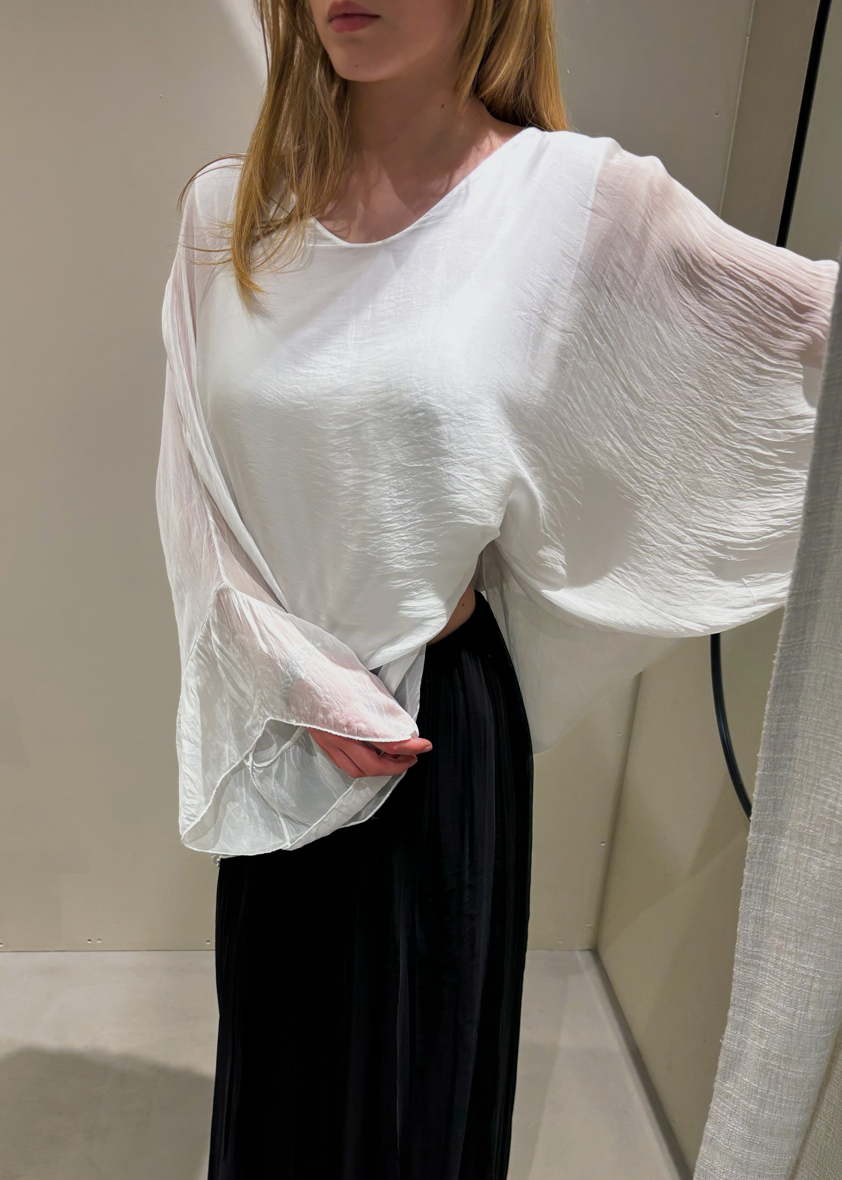 Person wearing a white blouse and black pants in a minimal indoor setting
