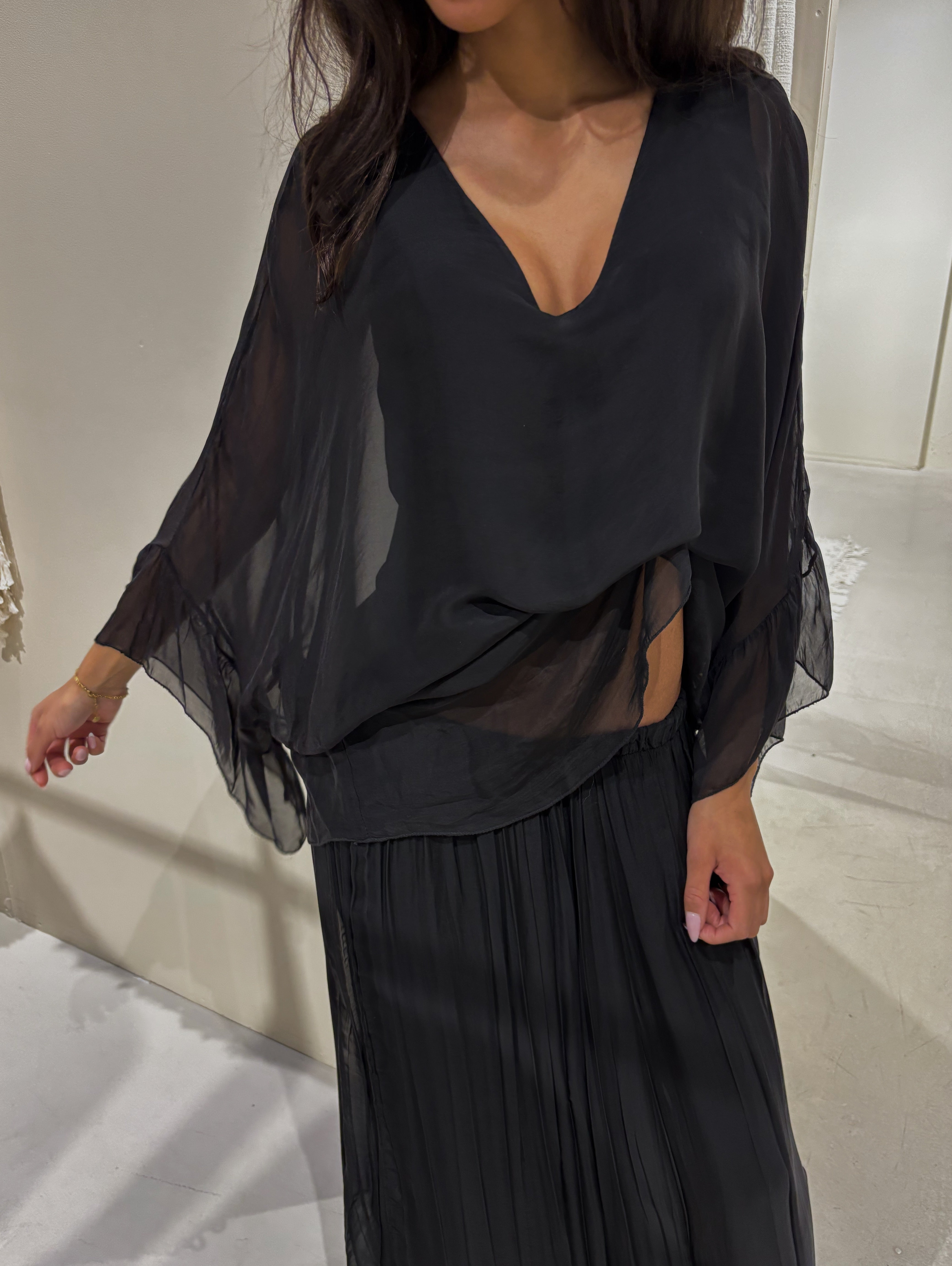 Person wearing a black outfit with sheer sleeves against a neutral background