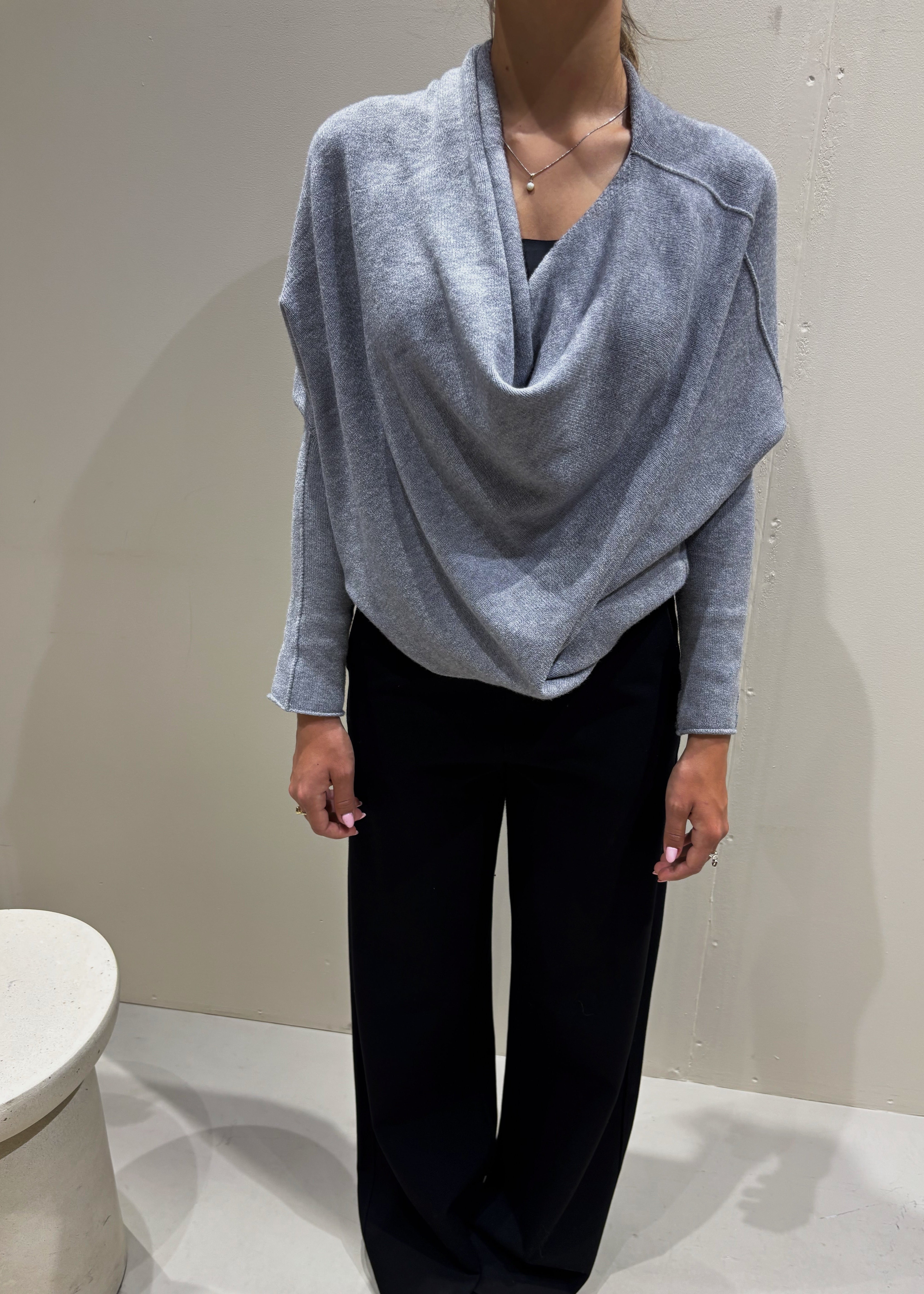 Person wearing a light gray sweater and black pants against a plain background