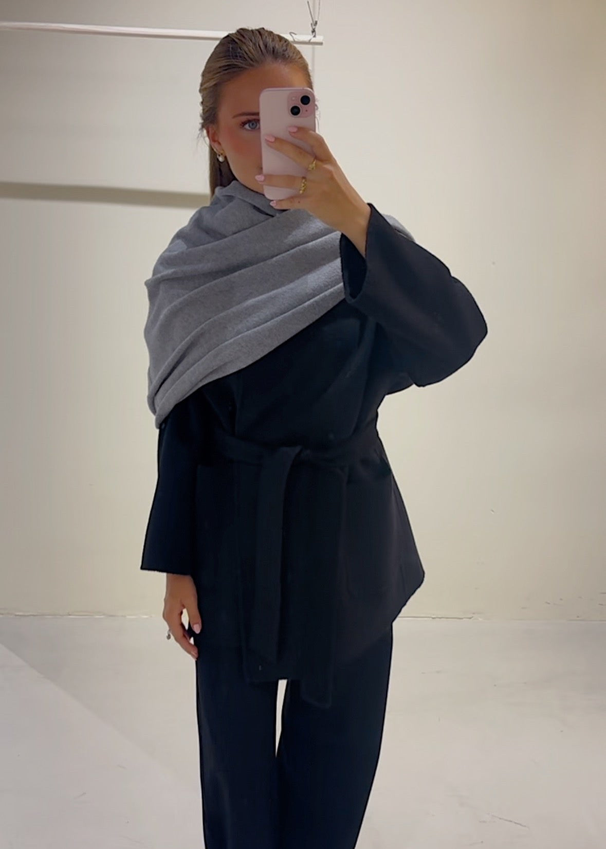 Person wearing a black outfit with a gray scarf in a minimal indoor setting