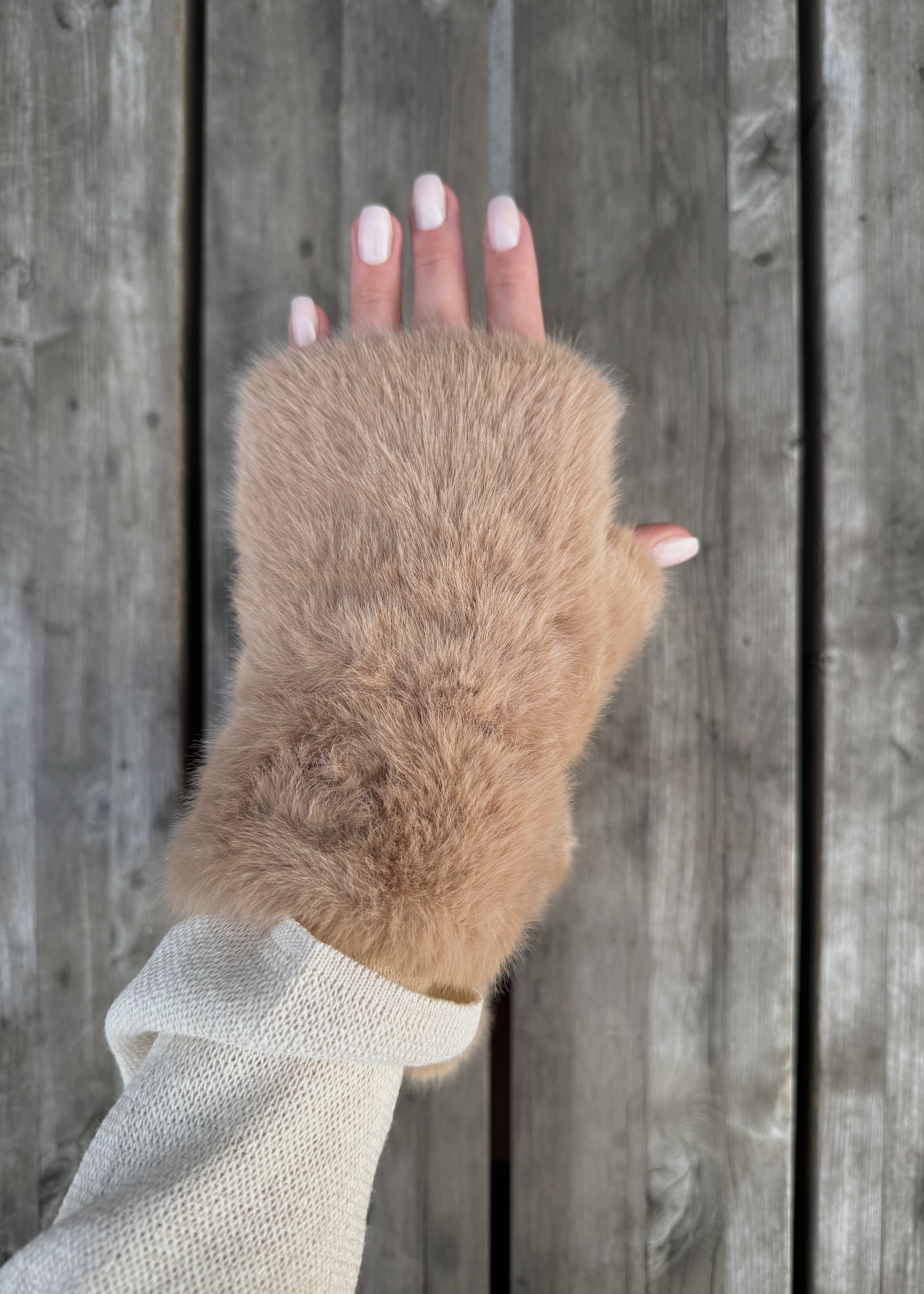 Hand wearing a fur wrist warmer against a wooden background