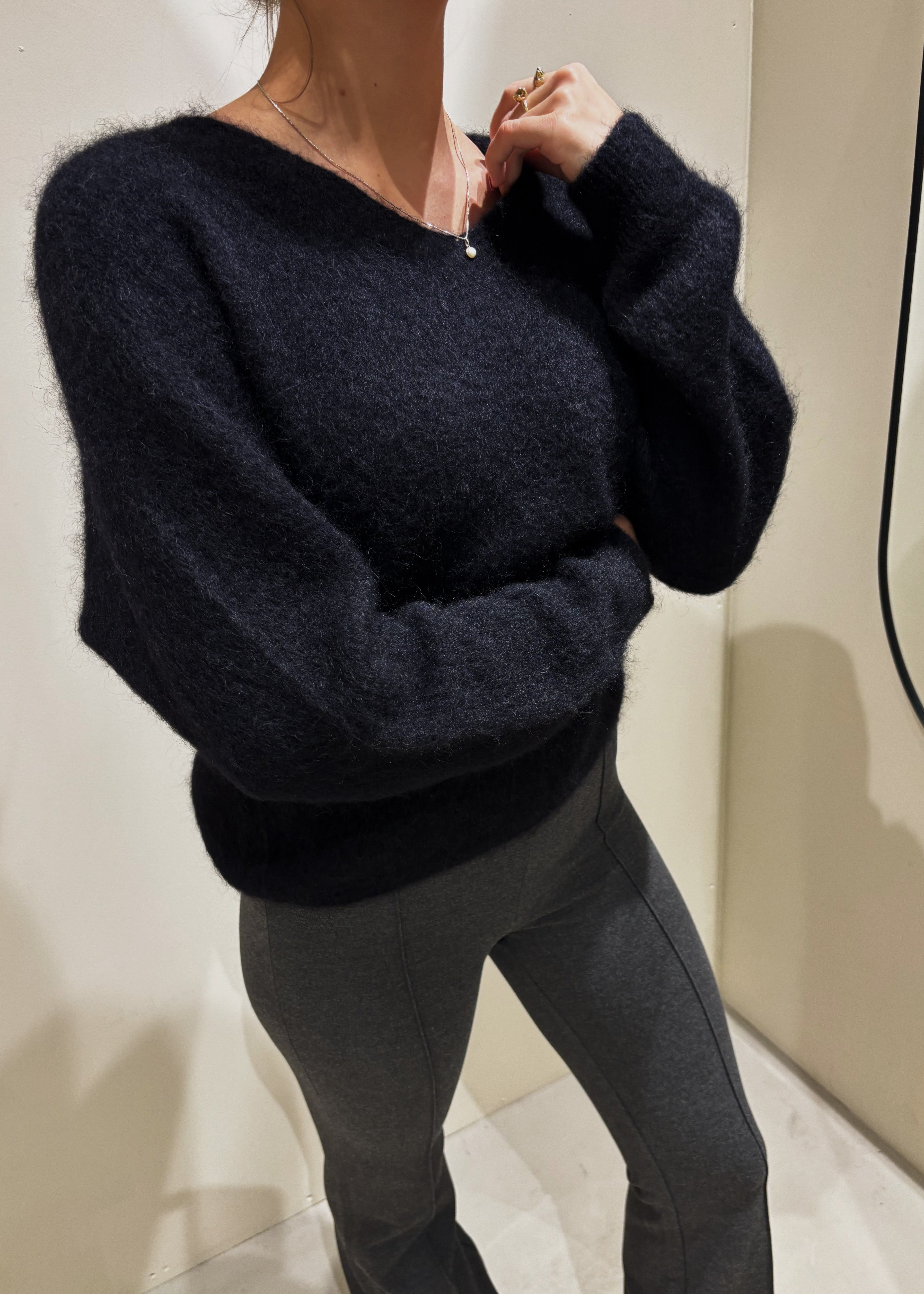 Person wearing a dark blue sweater and black pants in a neutral setting