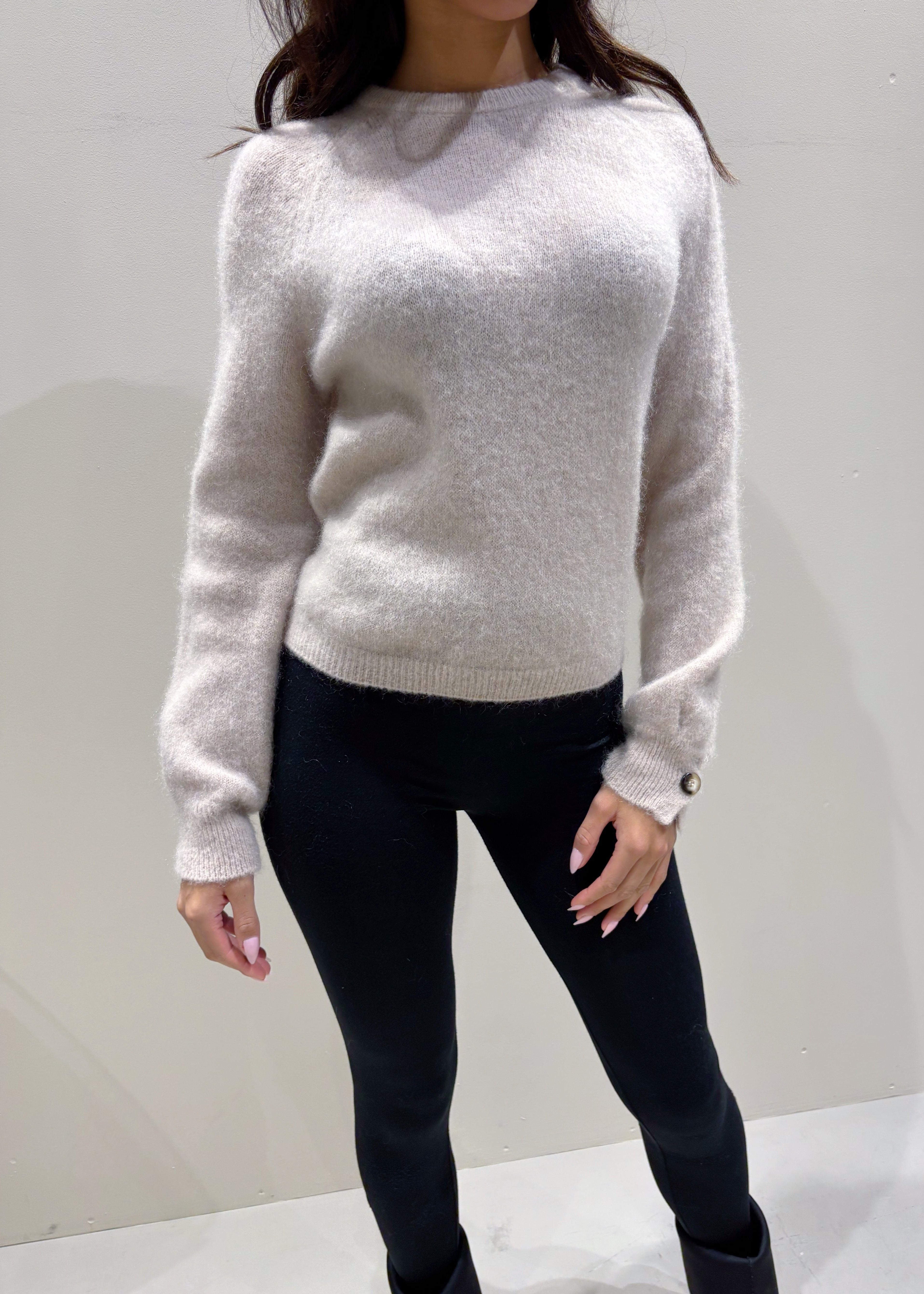Person wearing a light gray sweater and black pants against a white background