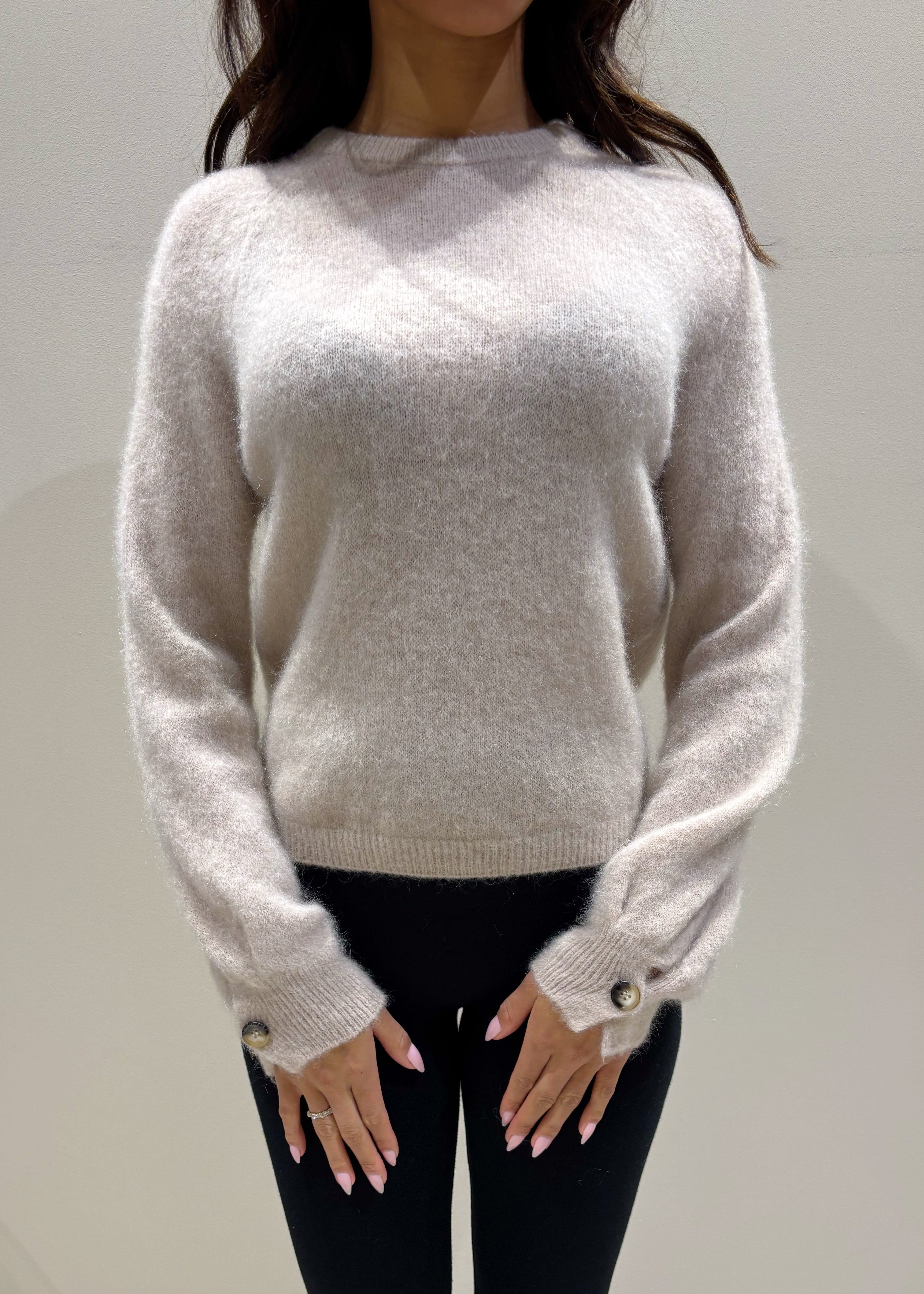 Person wearing a sand sweater and dark pants against a plain background