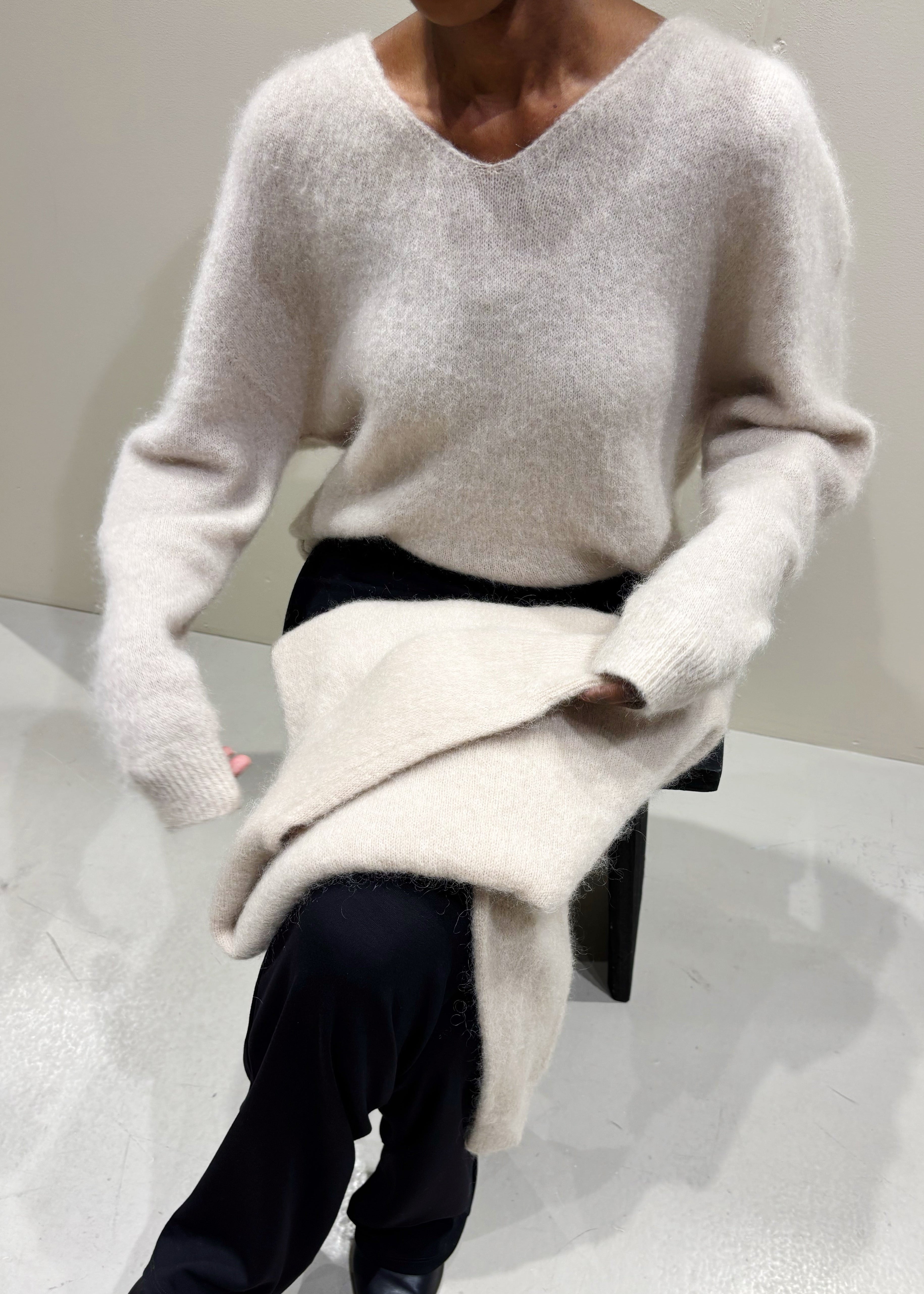 Person wearing a white sweater and black pants sitting on a white surface.