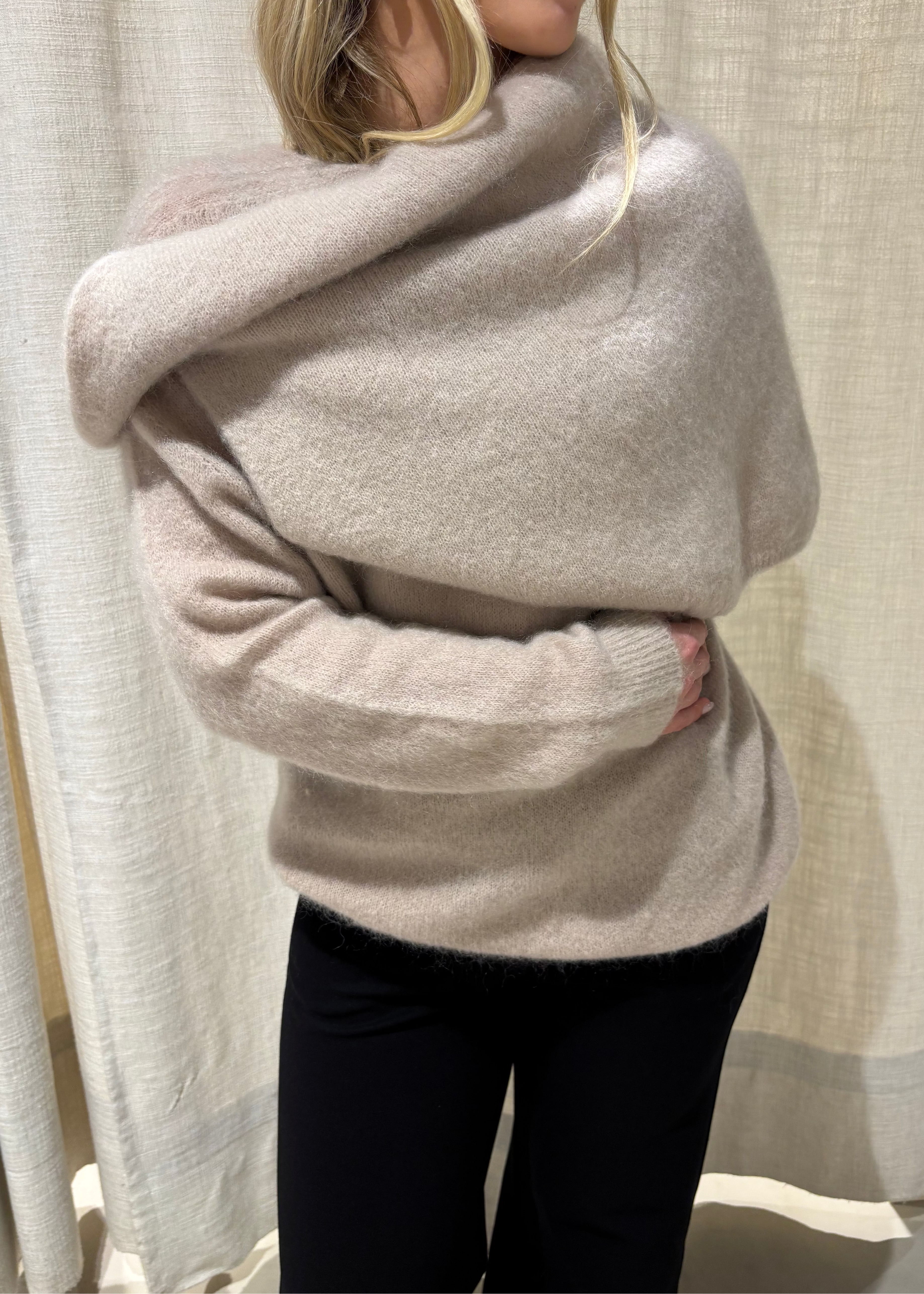 Woman wearing a beige sweater and black pants against a neutral background