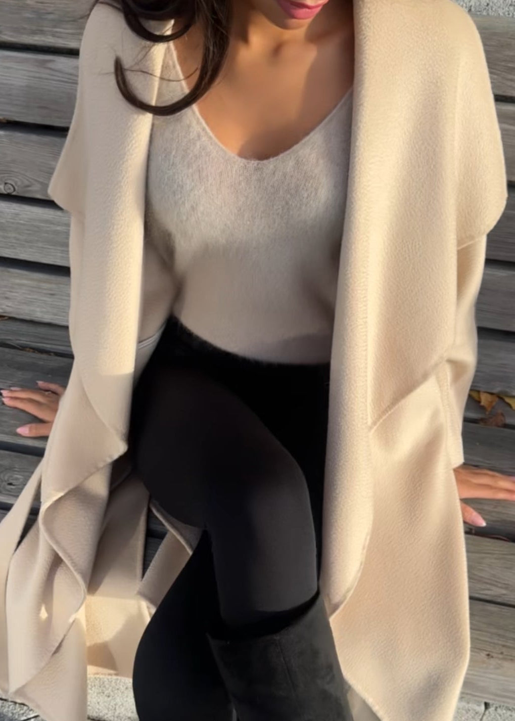 Person wearing a beige cardigan, white top, and black leggings outdoors on a wooden deck.