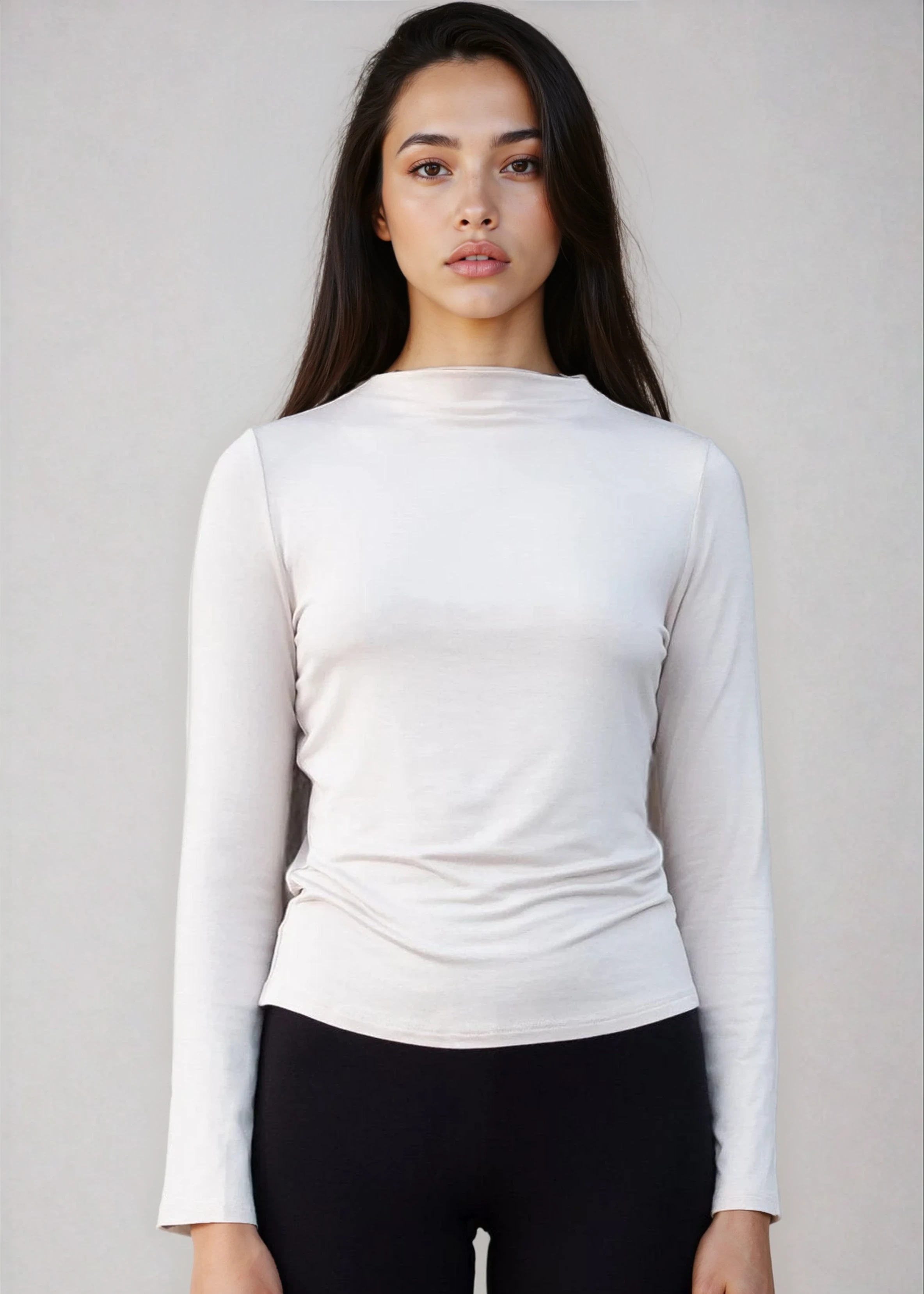 Woman wearing a white long-sleeve top and black pants against a plain background